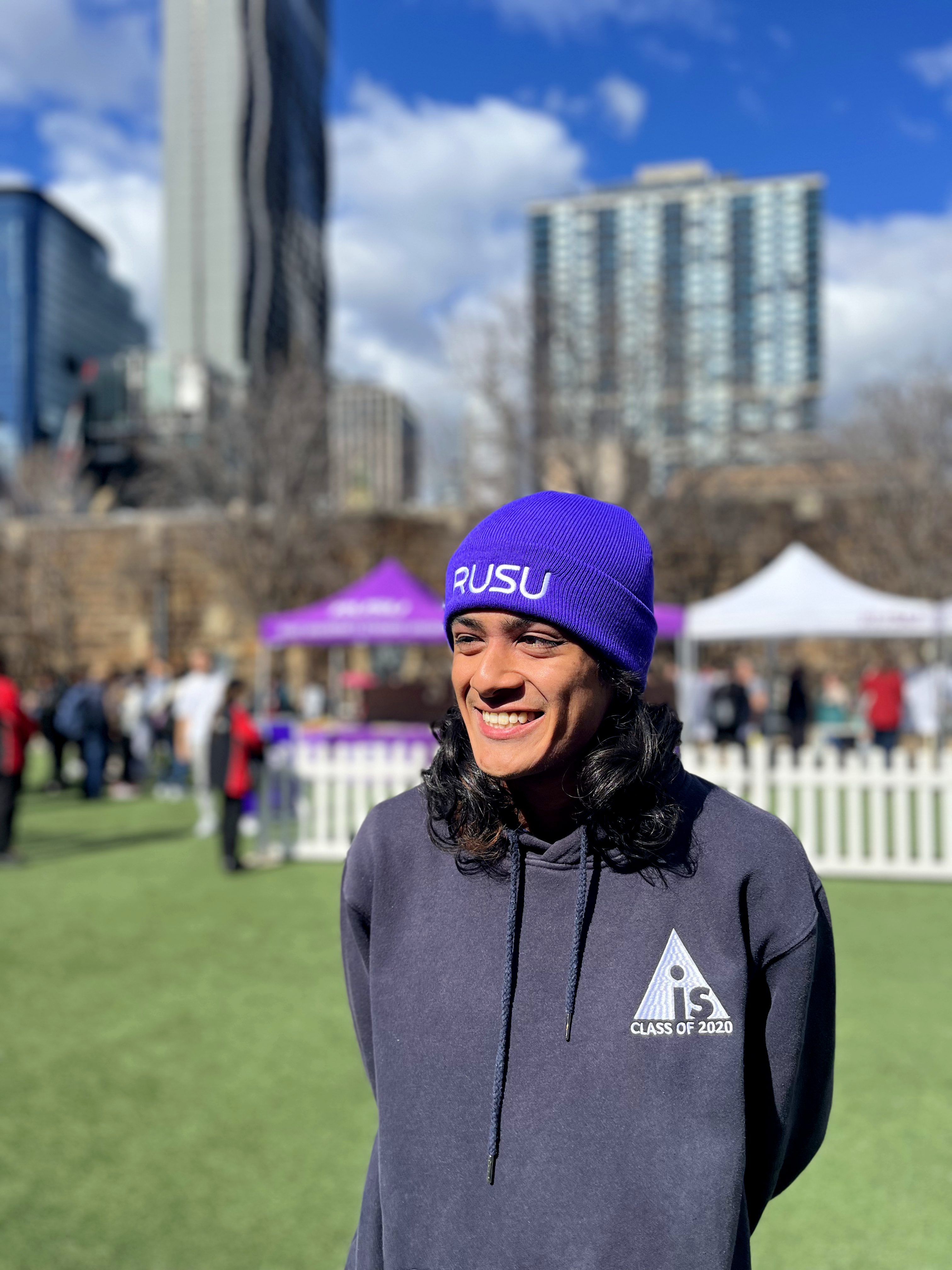 A smiling model wearing the Purple RUSU Beanie with white embroidered logo in an outdoor setting, available at the RMIT Store.
