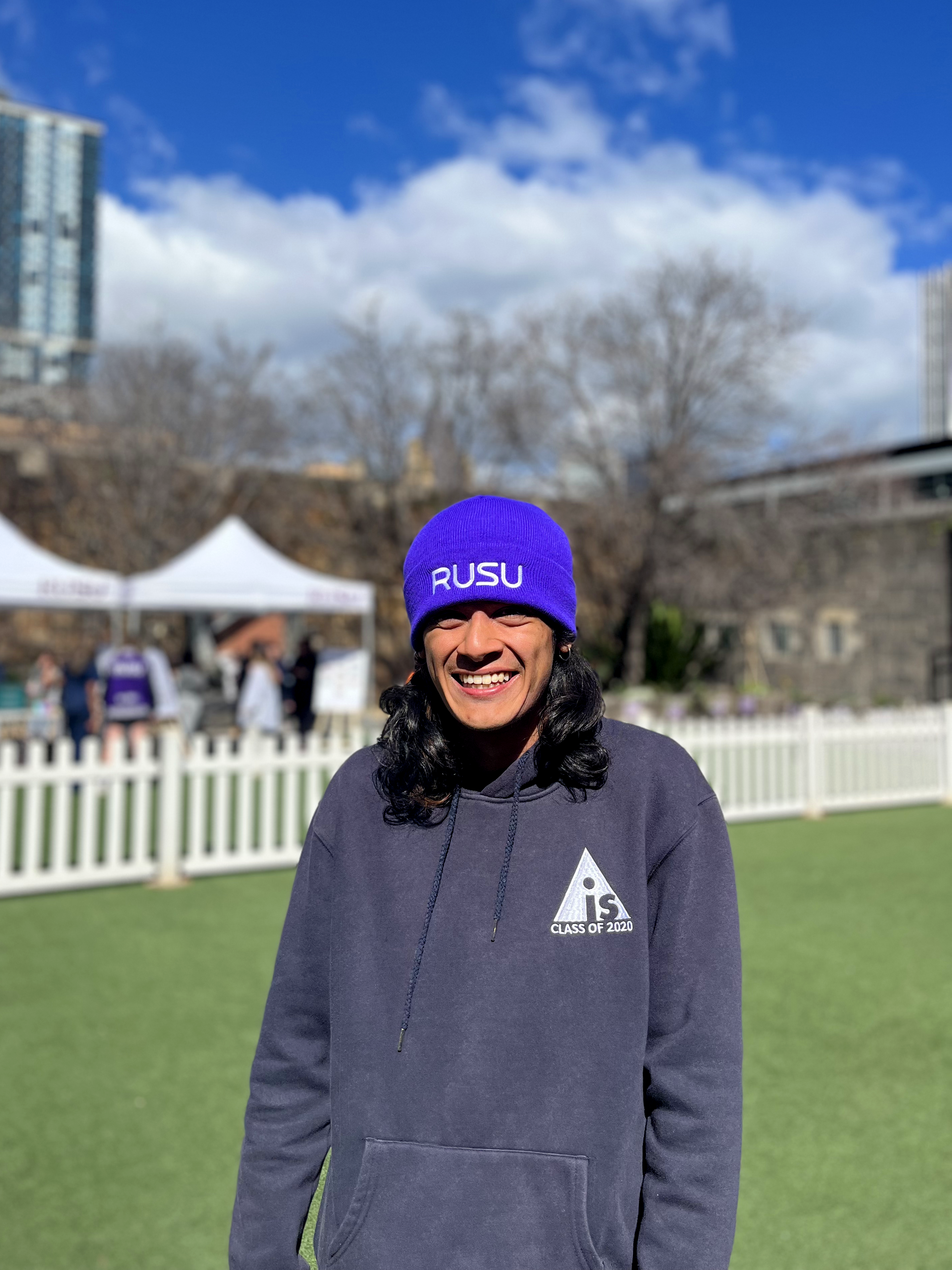 Model wearing the Purple RUSU Beanie with white embroidered logo in an outdoor setting, available at the RMIT Store.