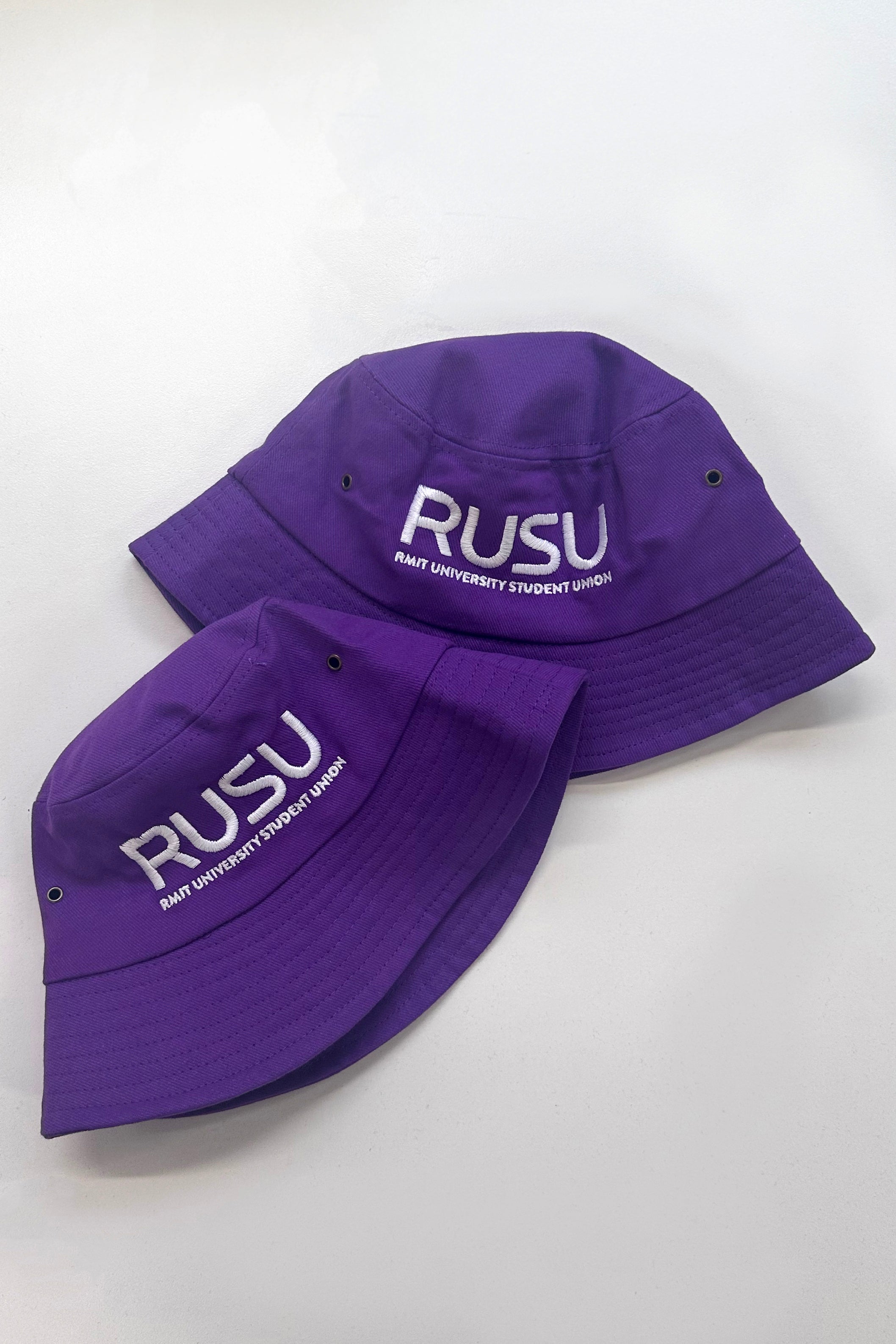 Close-up of two purple RUSU bucket hats with RMIT University Student Union logo, showcasing the hats' durable materials and vivid colours. Part of the RMIT Store collection, these hats are perfect for showing school spirit.