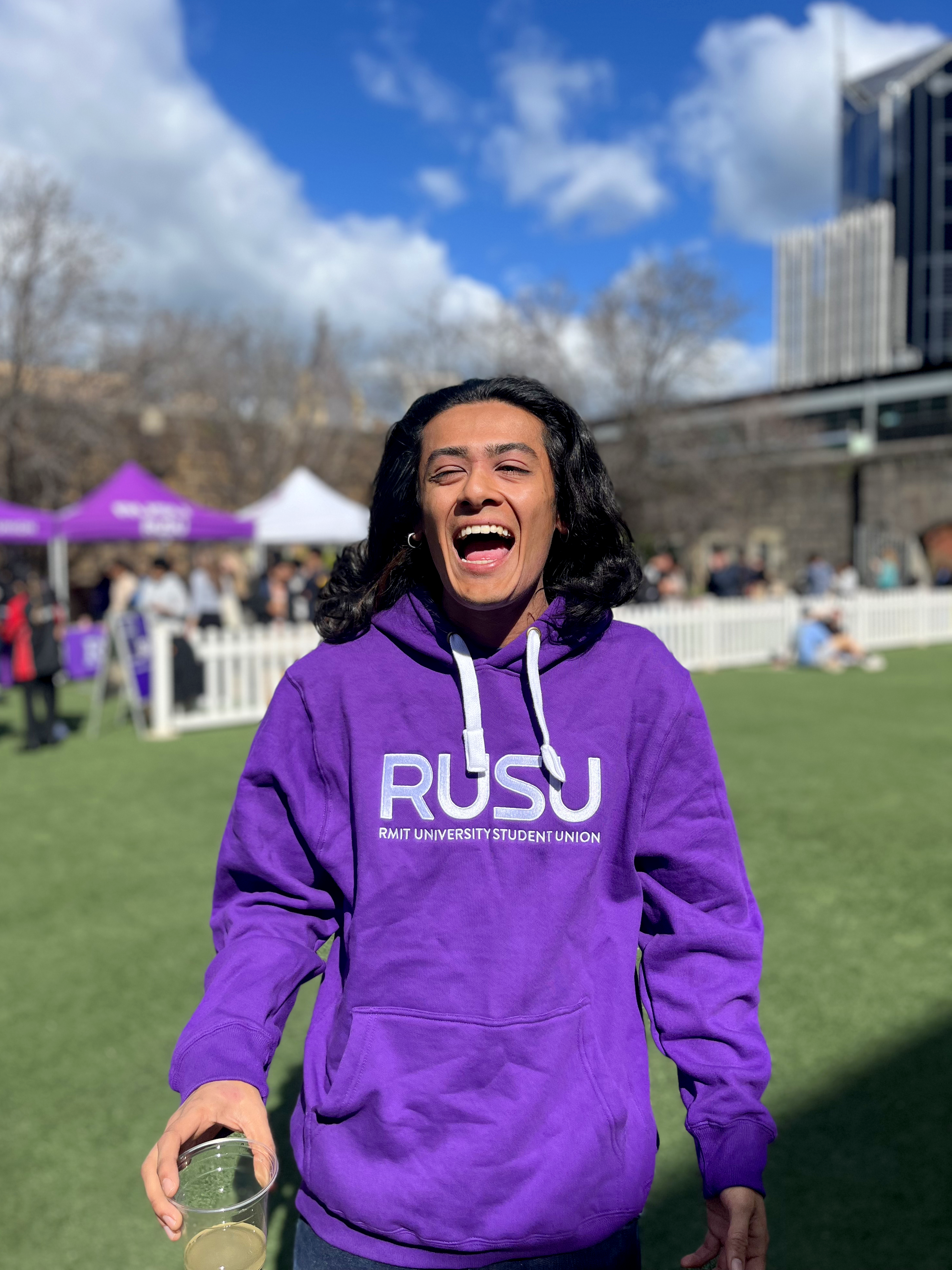 RUSU Hoodie in purple with large embroirdered white RUSU logo in centre chest. Modelled by student on Alumni Courtyard lawn at RMIT University in the Melbourne CBD.