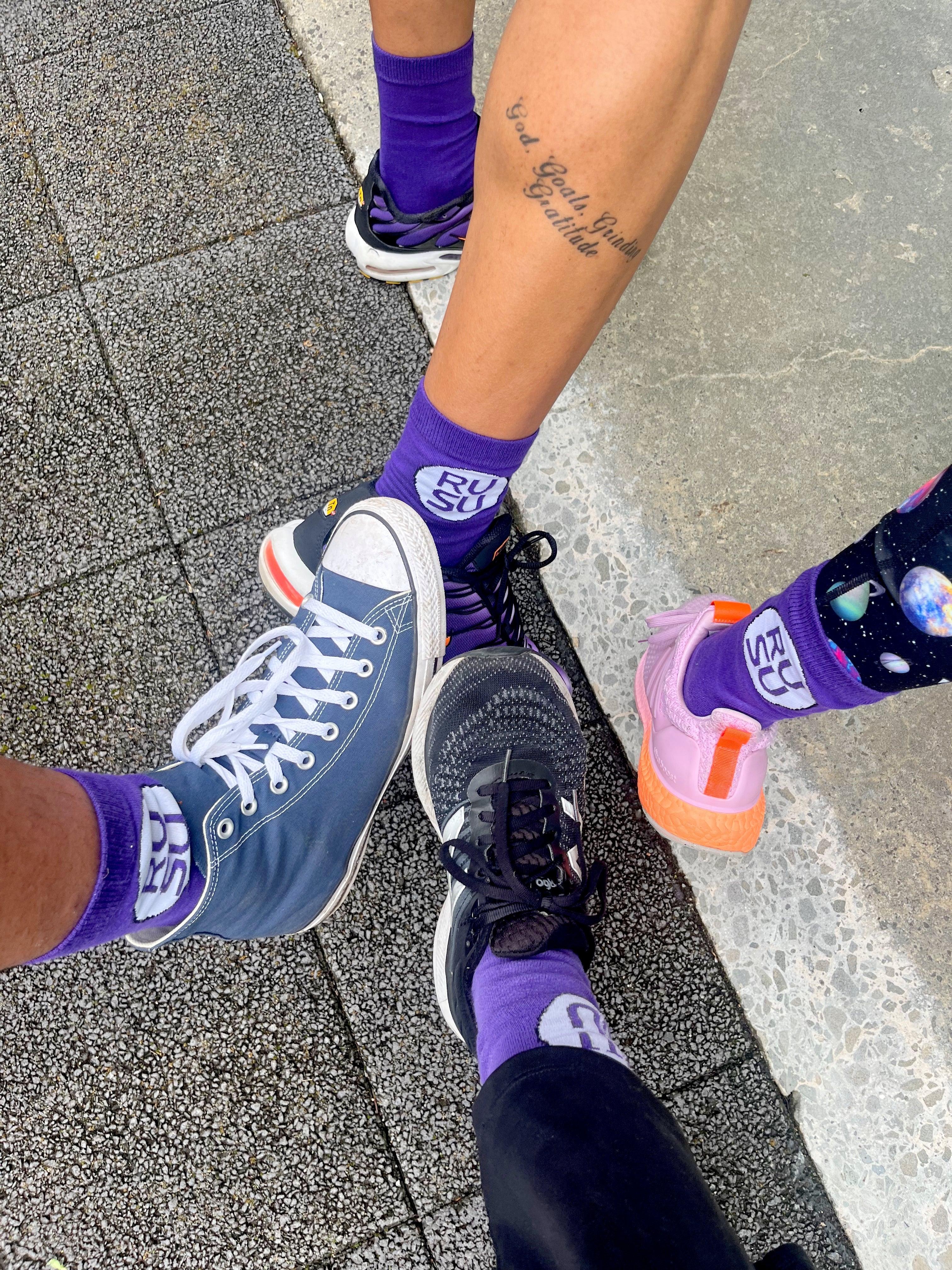 RUSU Socks in purple with a white circle with the RUSU logo. Worn in a group shot of 4 models.
