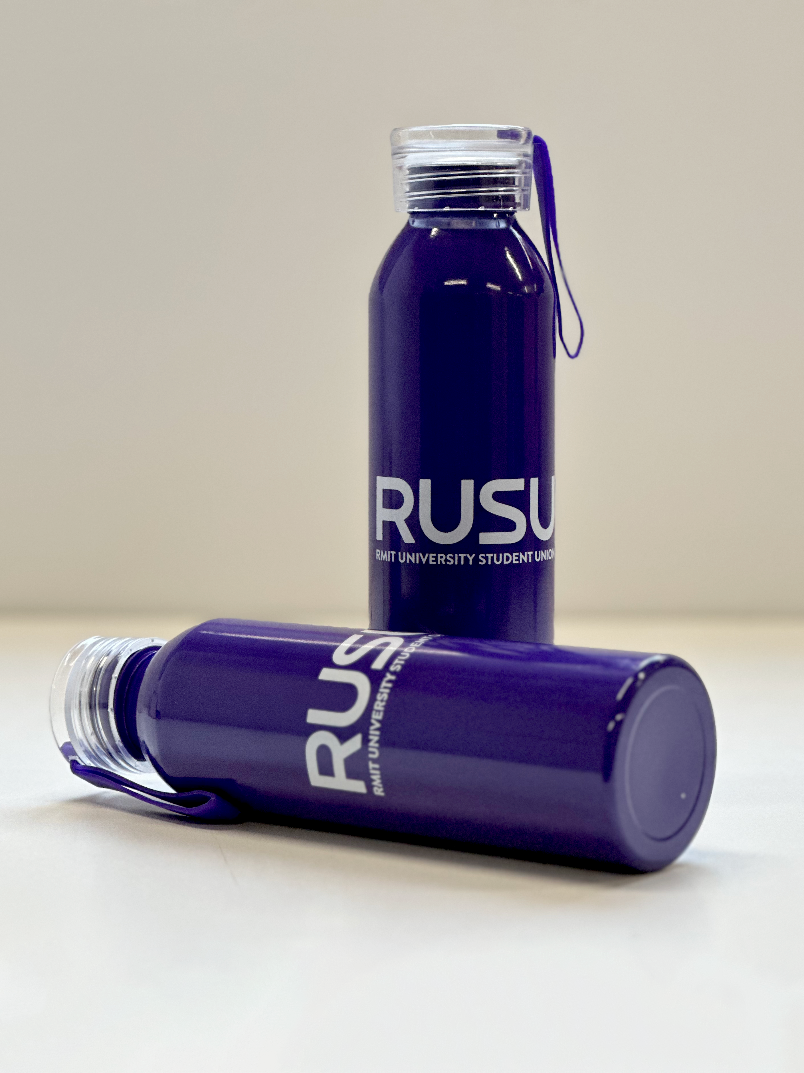 RUSU Water Bottle in puprple with a white printerd RUSU logo. One bottle standing and one bottle lying down on a surface.
