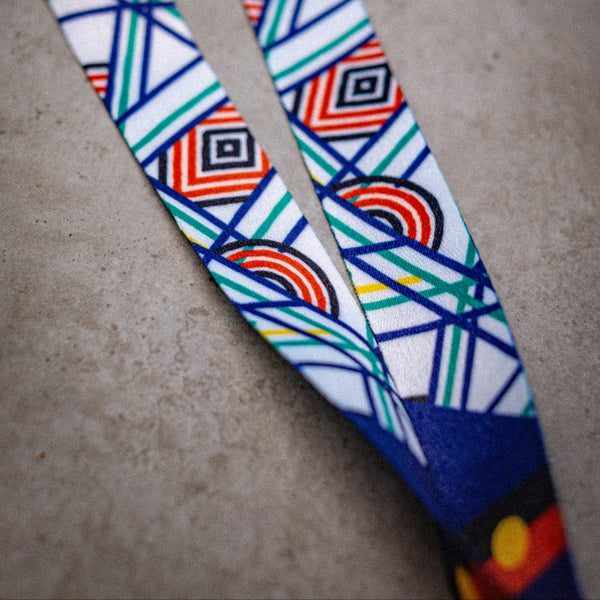 Sentient Lanyard displayed diagonally on a light surface, fully extended to show the entire Sentient linework in red, yellow, green, and blue symbolising sun, land, and sea. Available at RMIT Store.