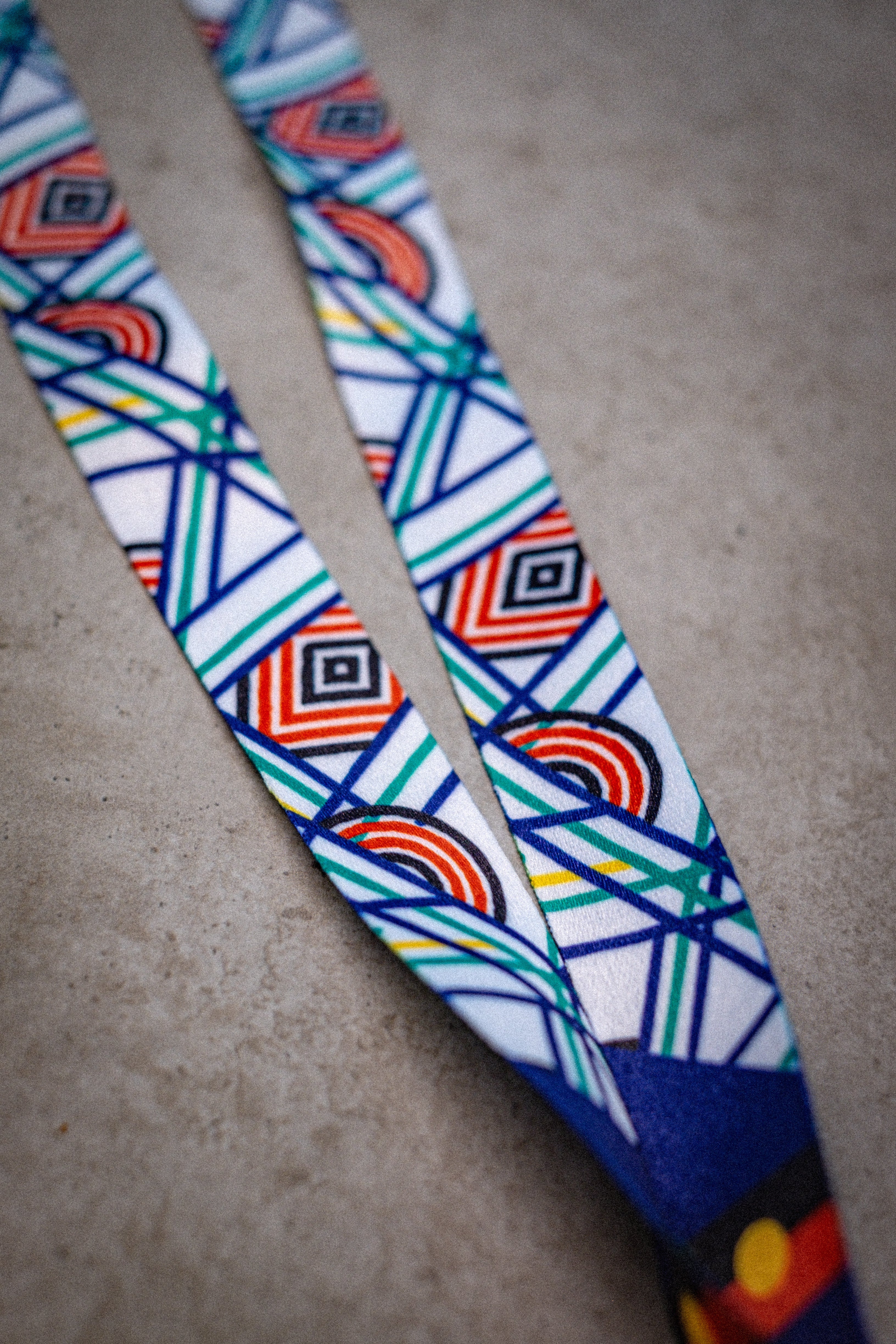 Sentient Lanyard displayed diagonally on a light surface, fully extended to show the entire Sentient linework in red, yellow, green, and blue symbolising sun, land, and sea. Available at RMIT Store.