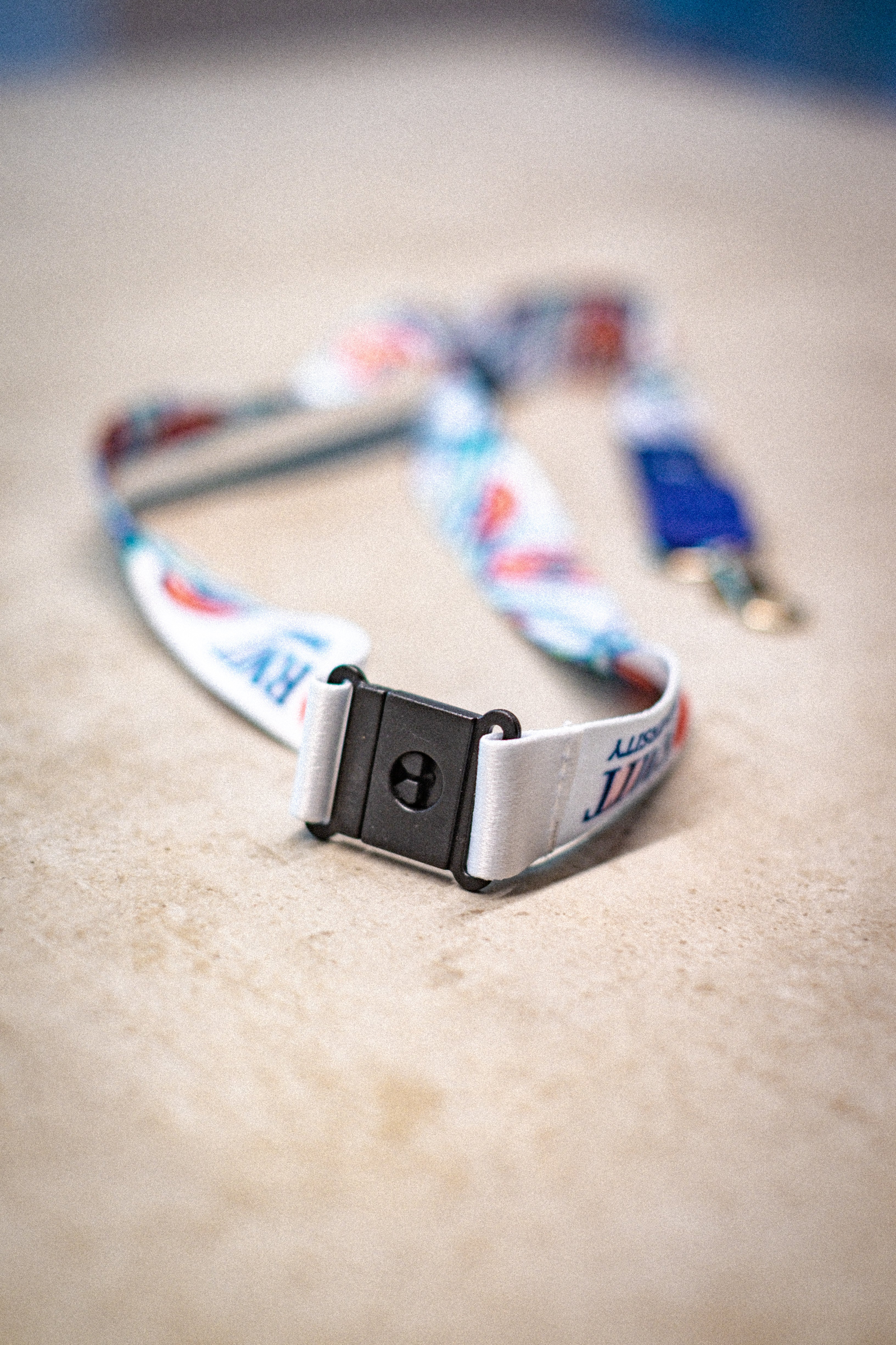 Top view of the Sentient Lanyard focusing on the silver swivel clip and black plastic buckle, with a partial view of the red, yellow, green, and blue flowing linework from the Sentient artwork. The visible section includes part of the “RMIT University” print. The lanyard is placed on a neutral-toned surface. Available at RMIT Store.