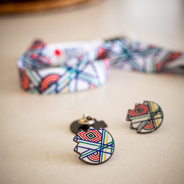 RMIT Store 'Sentient' lapel pin placed on a desk, showing colourful geometric patterns. A blurred 'Sentient' lanyard in the background complements the pin design, emphasising its artistic details and sharp metal finish.