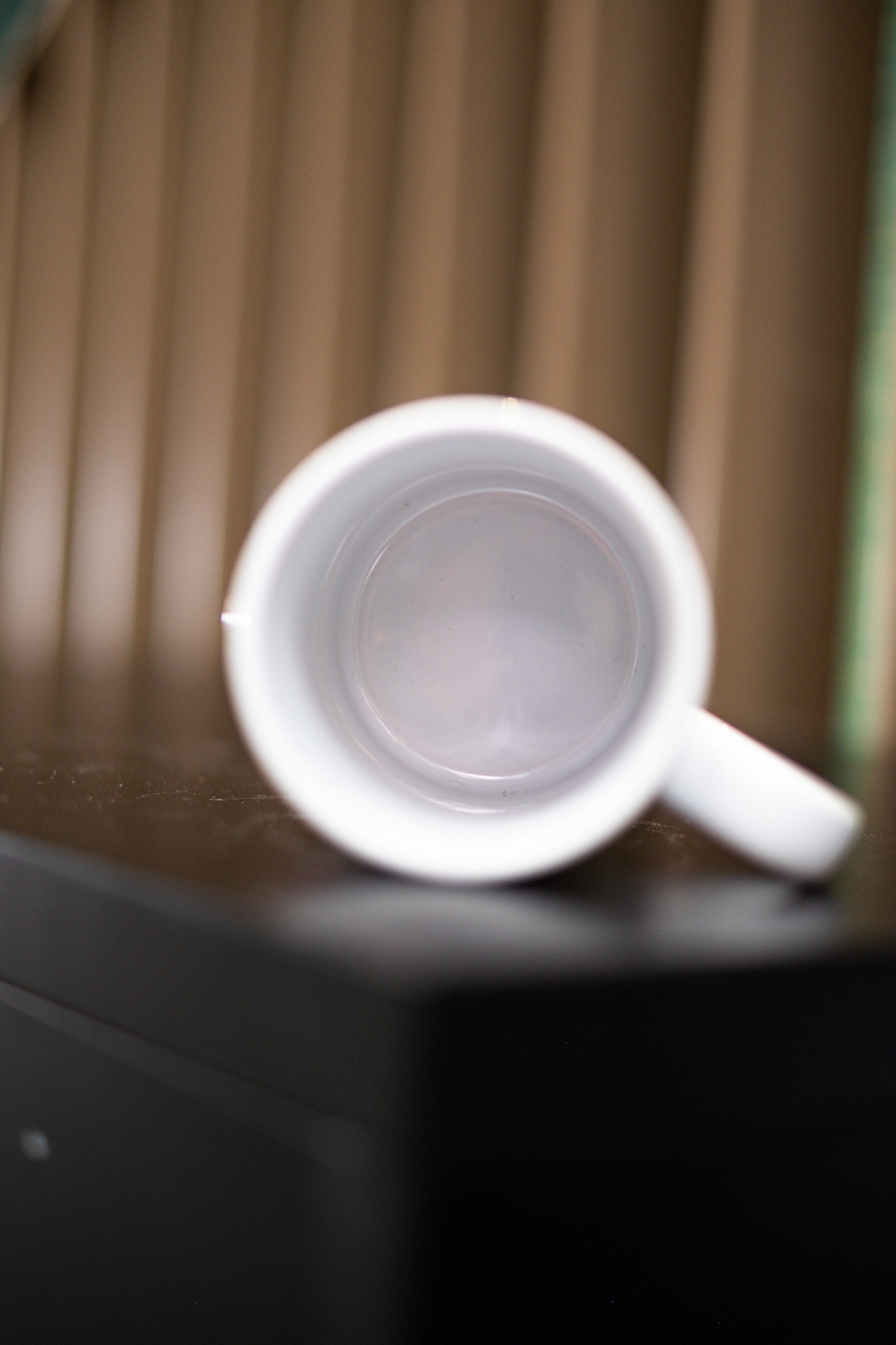 RMIT Store Sentient Mug, shown in a front view with the white ceramic mug laid flat on its back against a solid black surface. The glossy white interior is fully visible, and the handle is positioned to the right, emphasising the mug’s smooth, minimalist form and curved interior design.