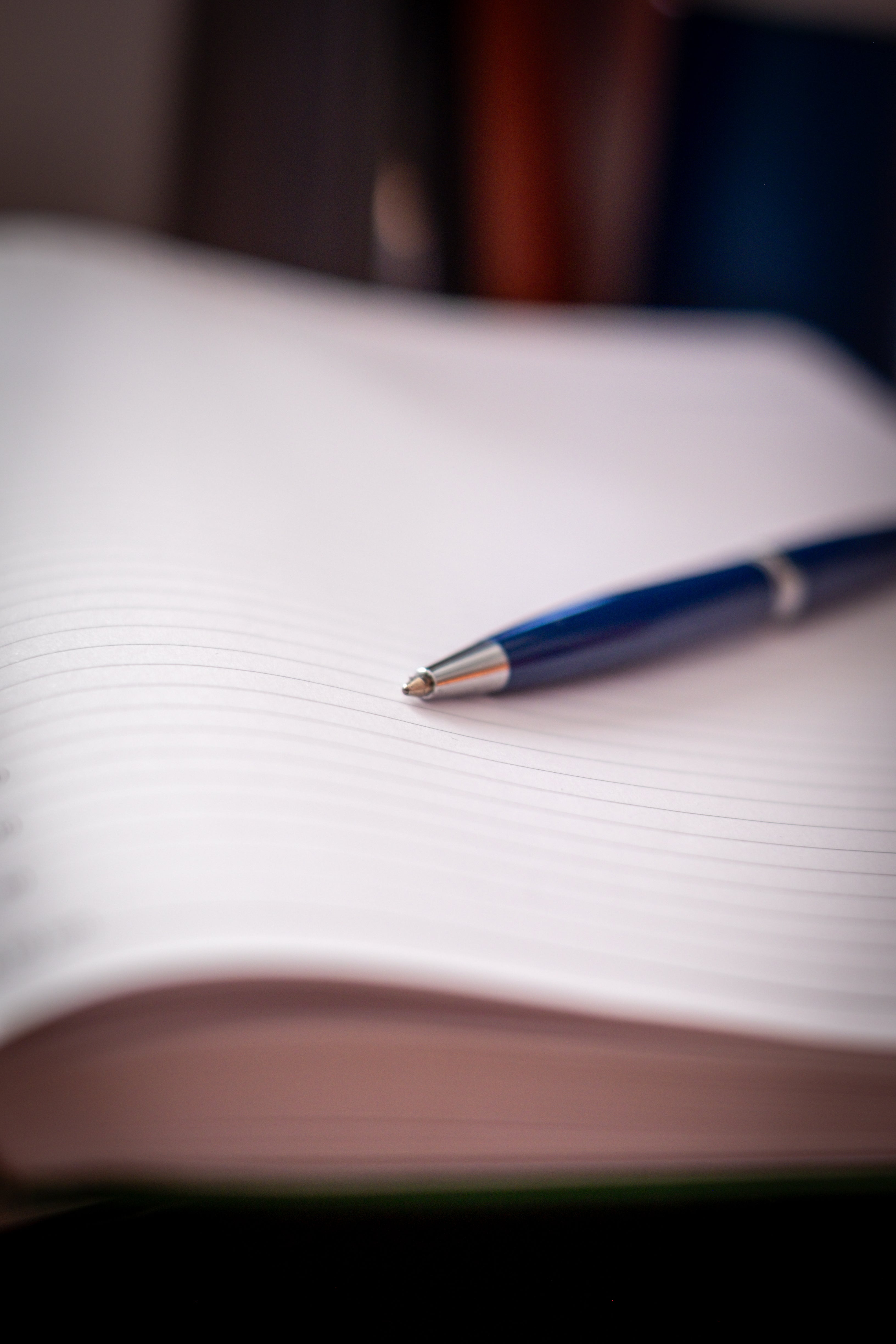 Navy RMIT Signature Pen with chrome accents and engraved RMIT University logo lying diagonally on a lined open notebook, photographed with shallow focus for the RMIT Store.