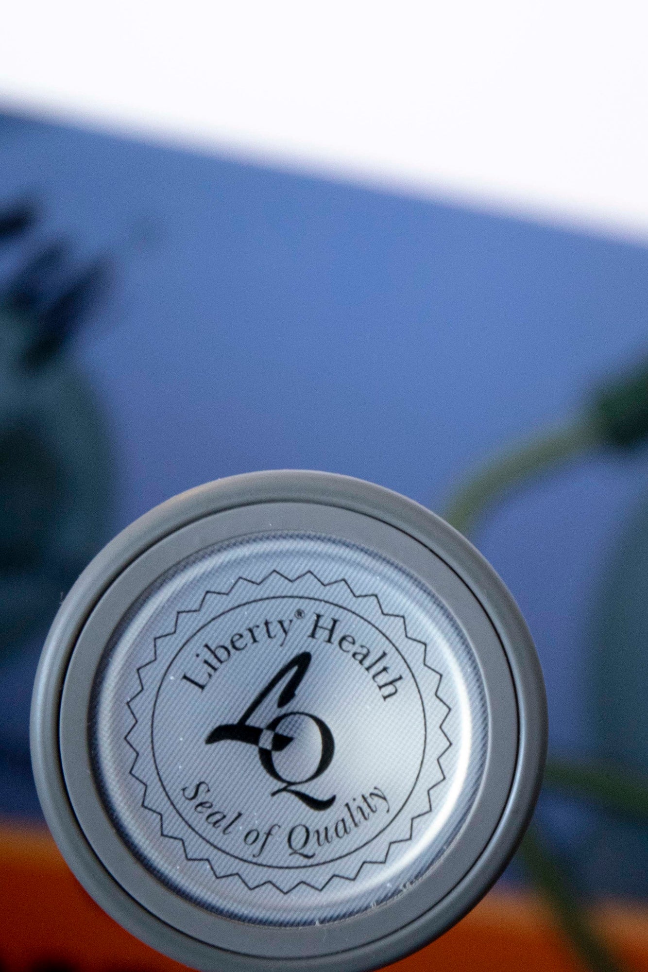 Close-up bottom view of a stethoscope showing the silver chest piece engraved with "Liberty Health" branding, attached to navy tubing with partially visible dark earpieces, displayed against a solid blue background. Available from the RMIT Store.