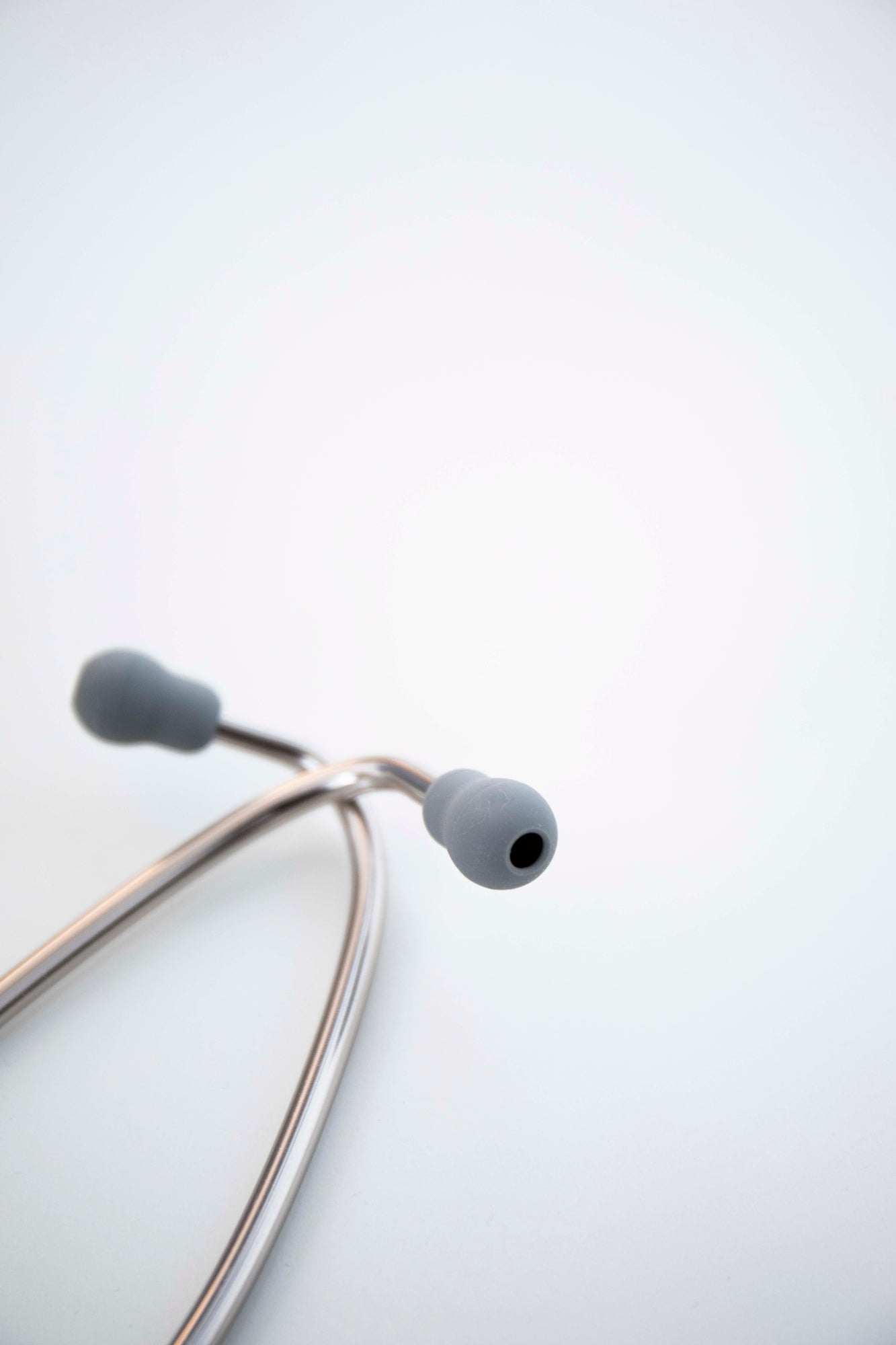 Close-up view of navy stethoscope earpieces with dark rubber tips and silver metal tubing, shown resting on a light grey surface. Available from the RMIT Store.