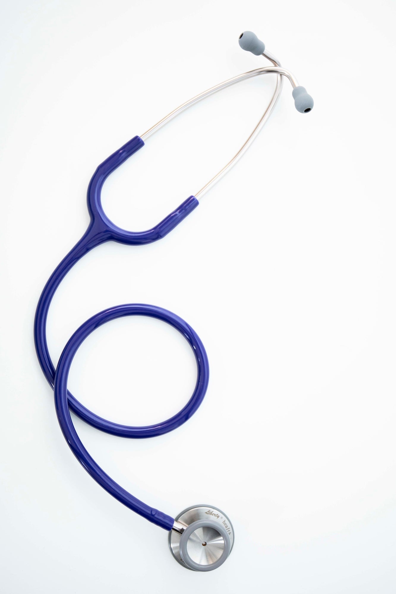Navy stethoscope with silver chest piece, navy tubing, and dark earpieces, arranged in a coiled position on a light white surface. The chest piece is clearly visible and resting at the base of the loop. This navy variant stethoscope is available from the RMIT Store.