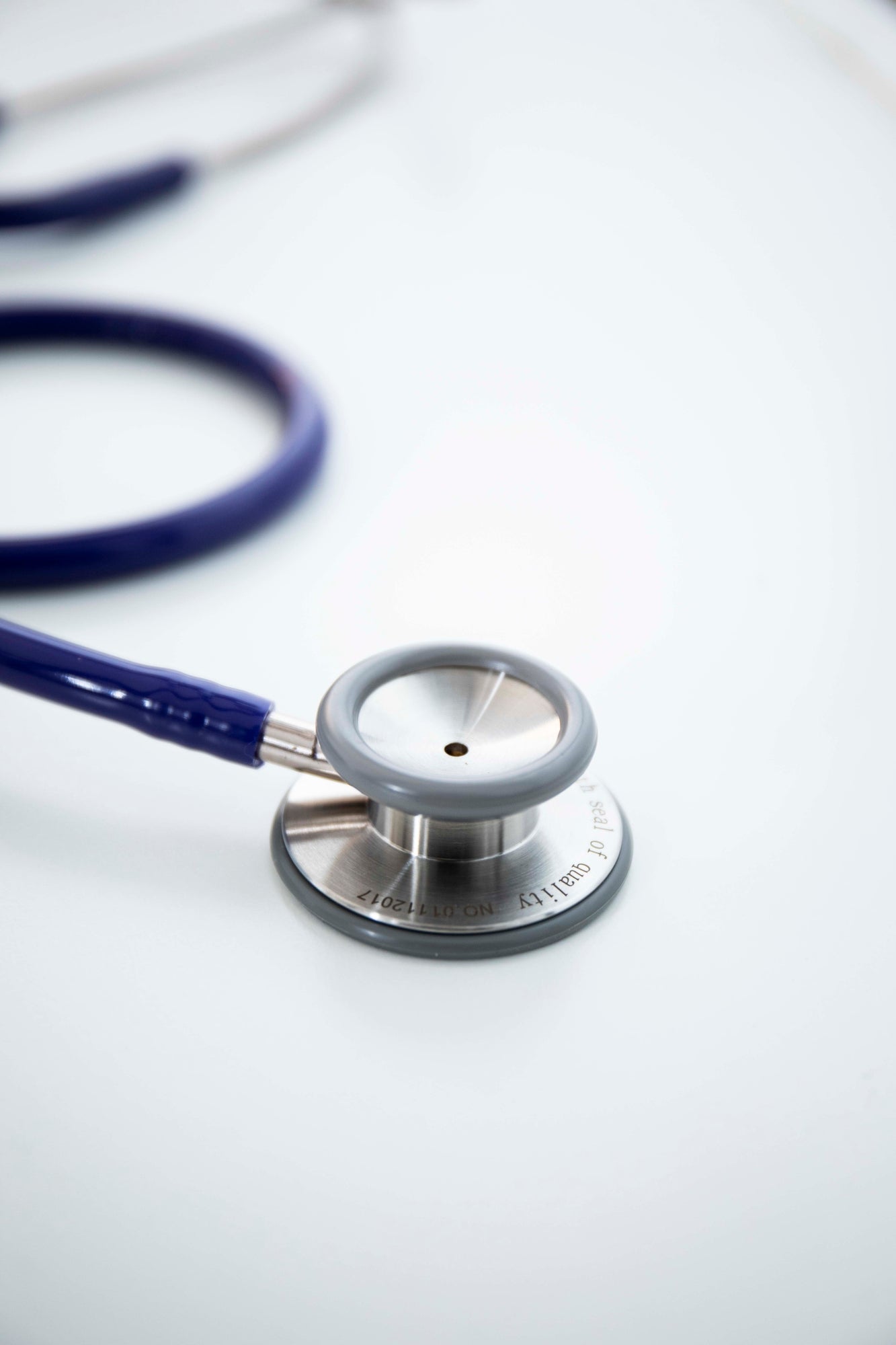 Navy stethoscope with silver chest piece and dark earpieces coiled neatly on a light white surface Available from the RMT Store.