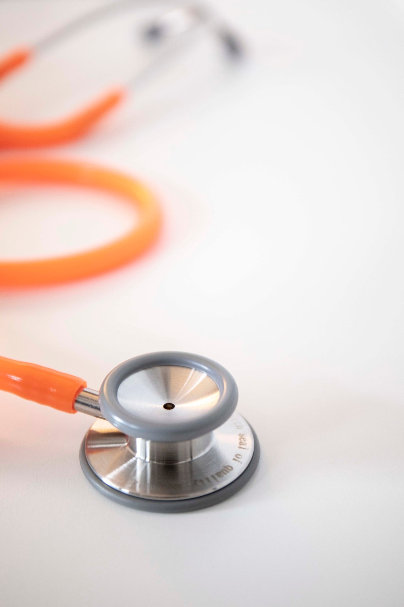 Orange stethoscope with silver chest piece, orange tubing, and dark earpieces, neatly coiled on a light grey surface. Available from the RMIT Store.