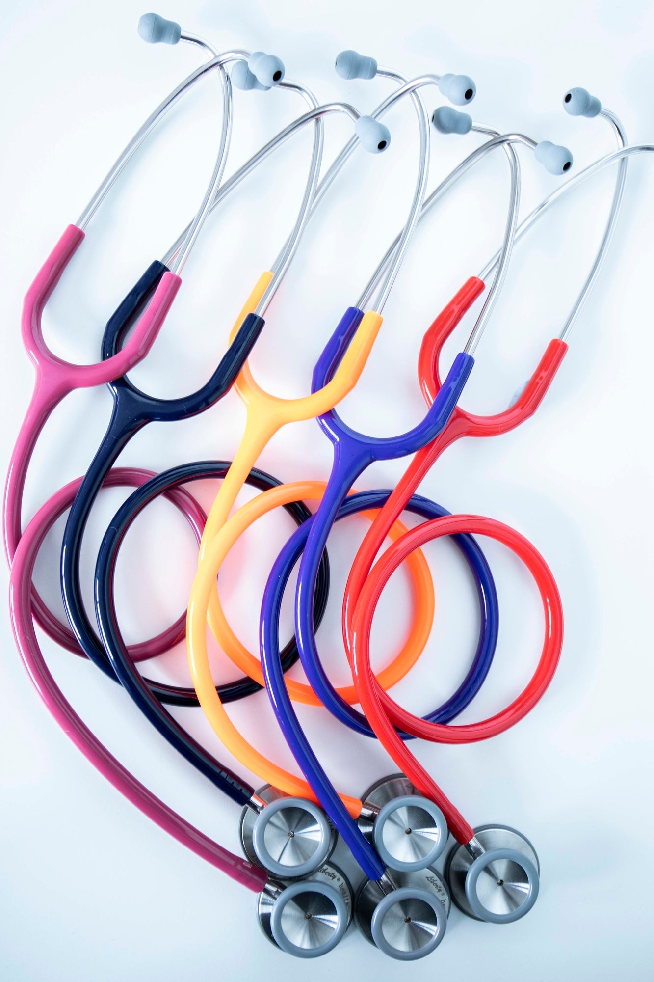 Full range of stethoscopes in various colours, including navy, purple, and orange, displayed together with dark earpieces and silver chest pieces. Each stethoscope features smooth tubing and is positioned against a light white background. Available from the RMIT Store.