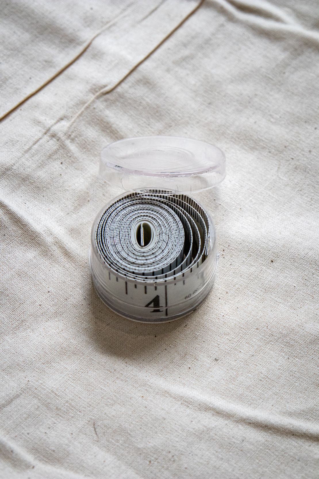 RMIT Store tape measure coiled neatly inside a transparent plastic case, set against a beige fabric backdrop for compact storage.
