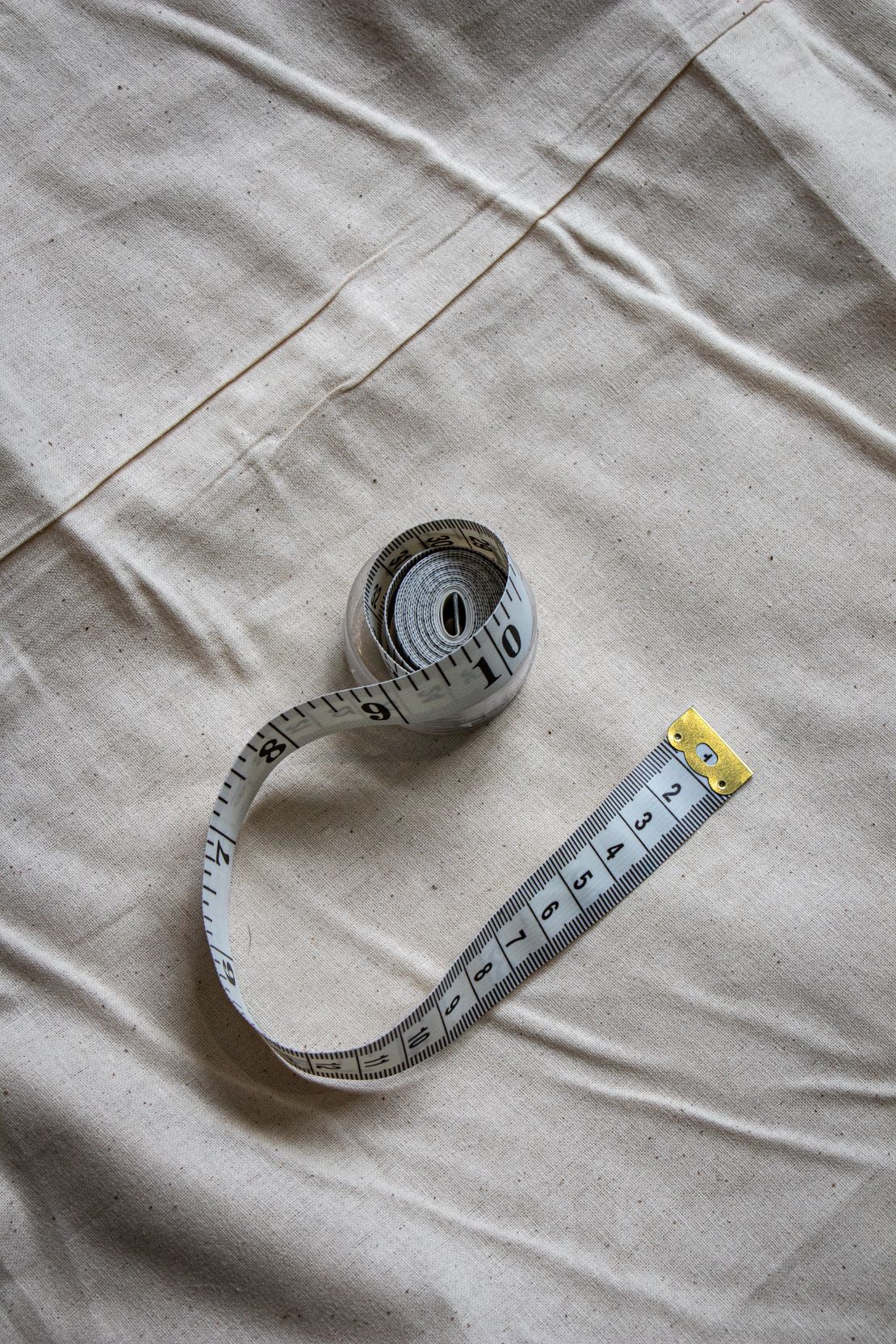 RMIT Store white tape measure with black numbers, shown fully extended on a neutral beige fabric, highlighting its flexibility and ease of use.