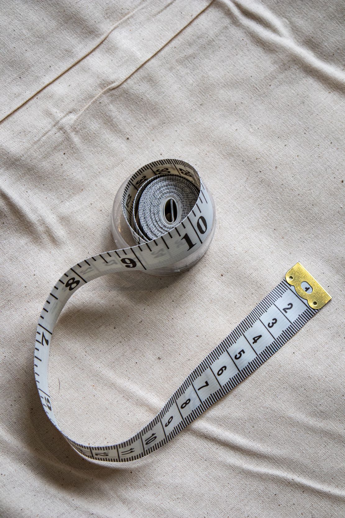 RMIT Store retractable tape measure extended to ten inches, placed on a beige fabric background. The tape is white with black markings, featuring a metal tab at the end.