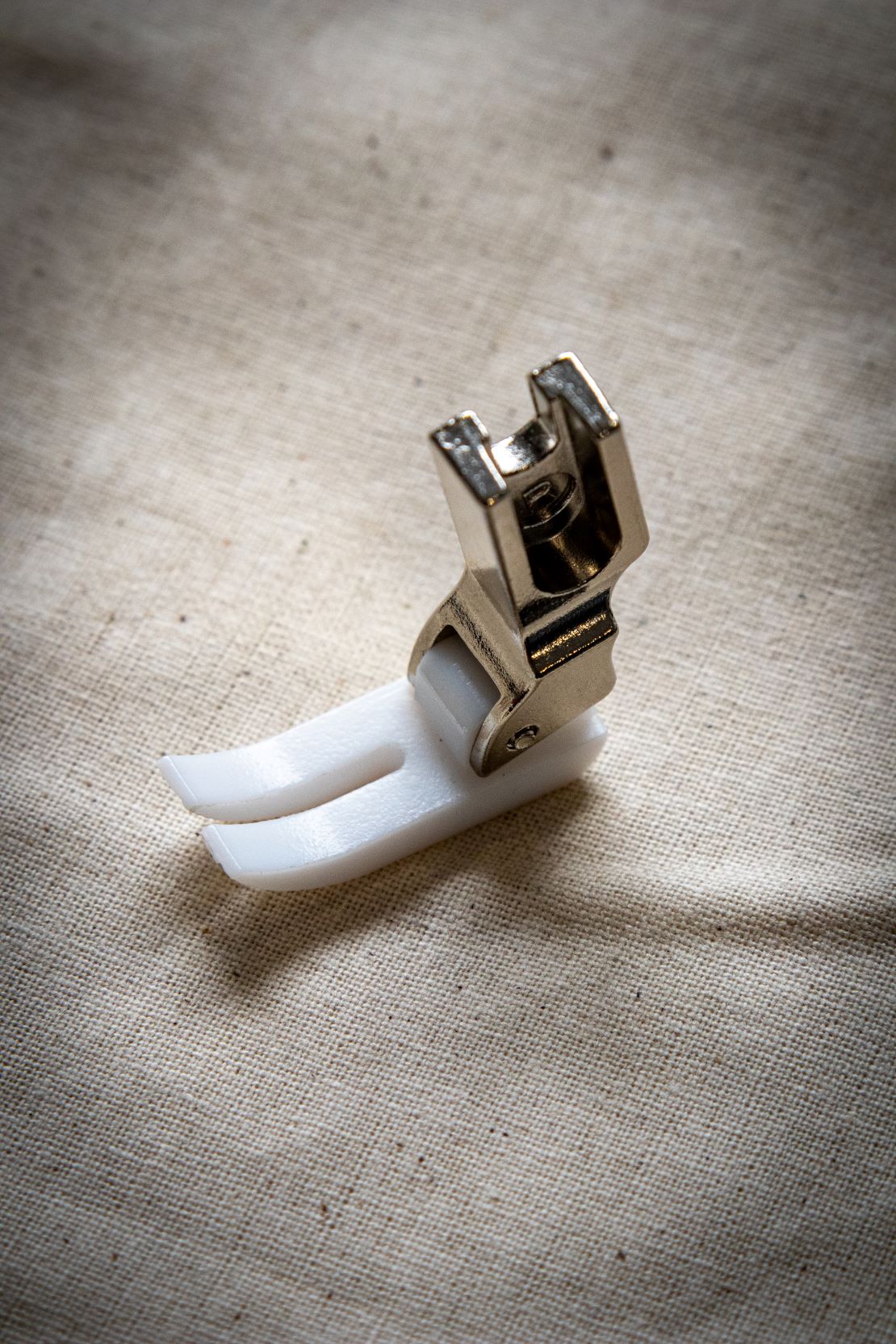 Top view of the Teflon presser foot from the RMIT Store, highlighting the clear plastic top and white non-stick underside, placed on beige fabric.