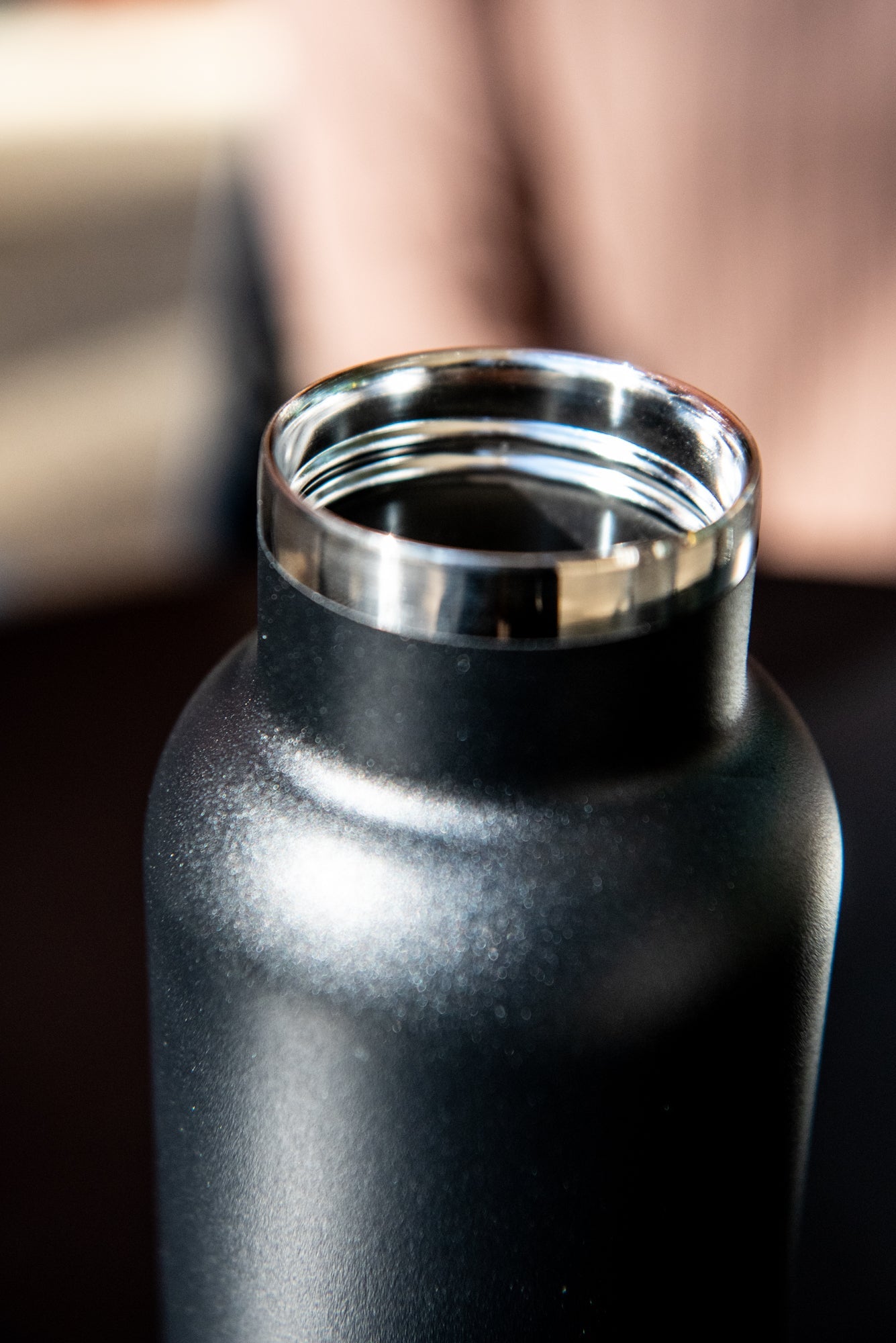 Close-up view of the top of the black RMIT Store 600ml thermo bottle with the lid removed, revealing the stainless steel interior. Bottle is placed on a black tabletop.