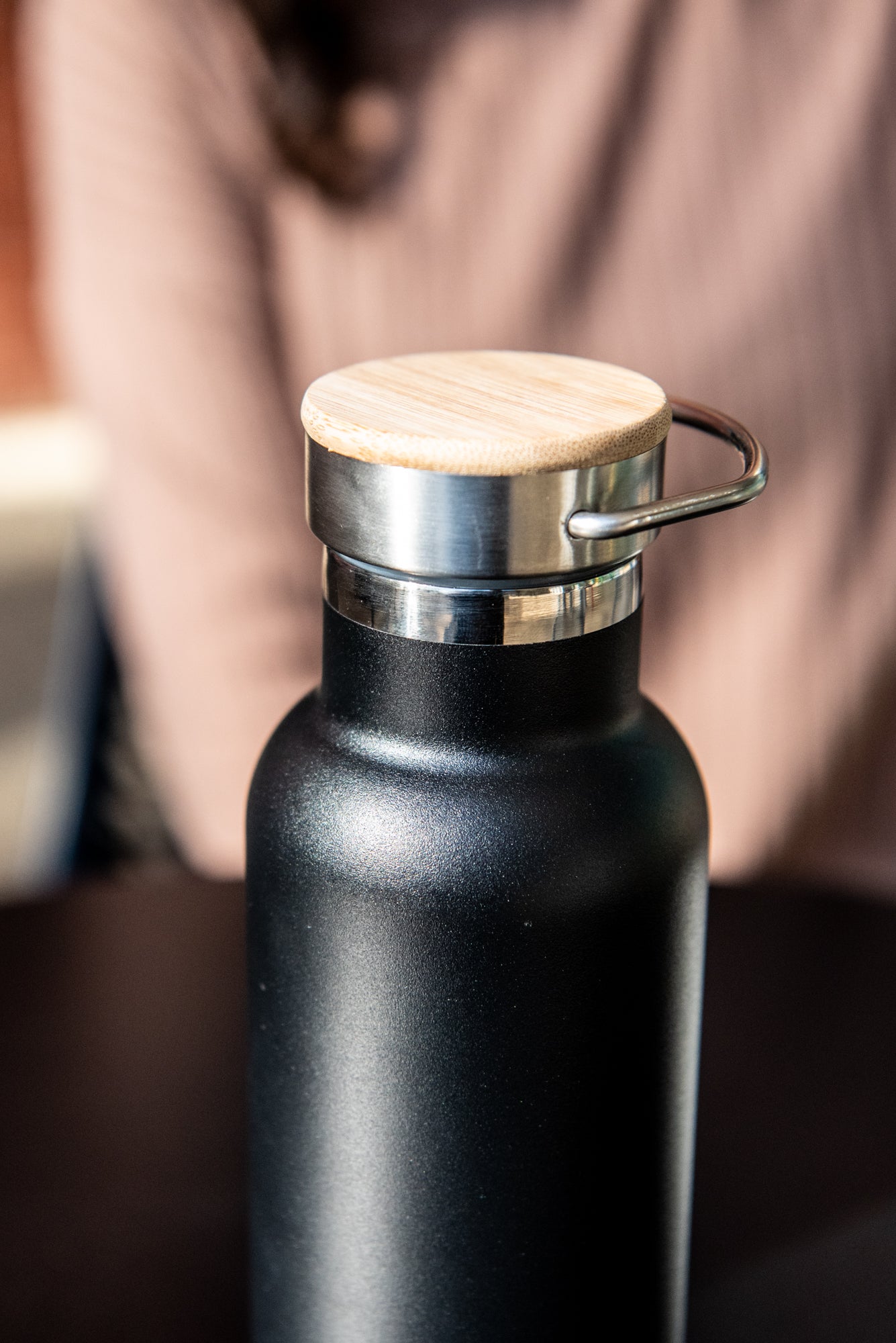 Top view of the black RMIT Store 600ml thermo bottle with the lid on, showcasing the stainless steel carry handle attached to the wooden lid. Bottle is positioned on a black tabletop.