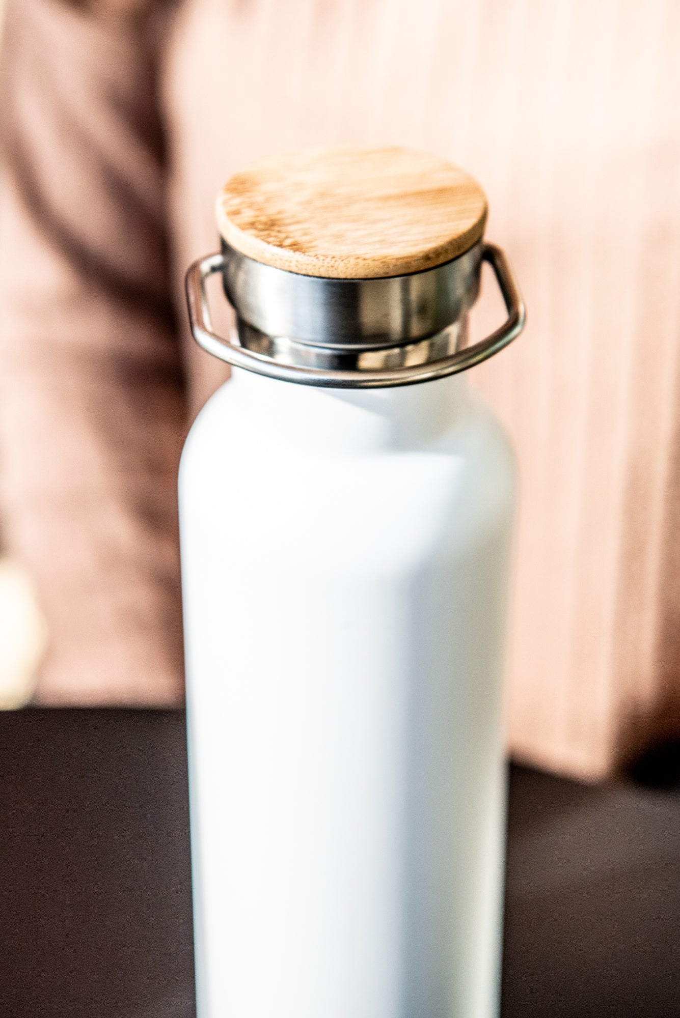 Top-down view of a white RMIT Store 600ml thermo bottle with its natural wood lid securely on. The bottle stands on a black tabletop.