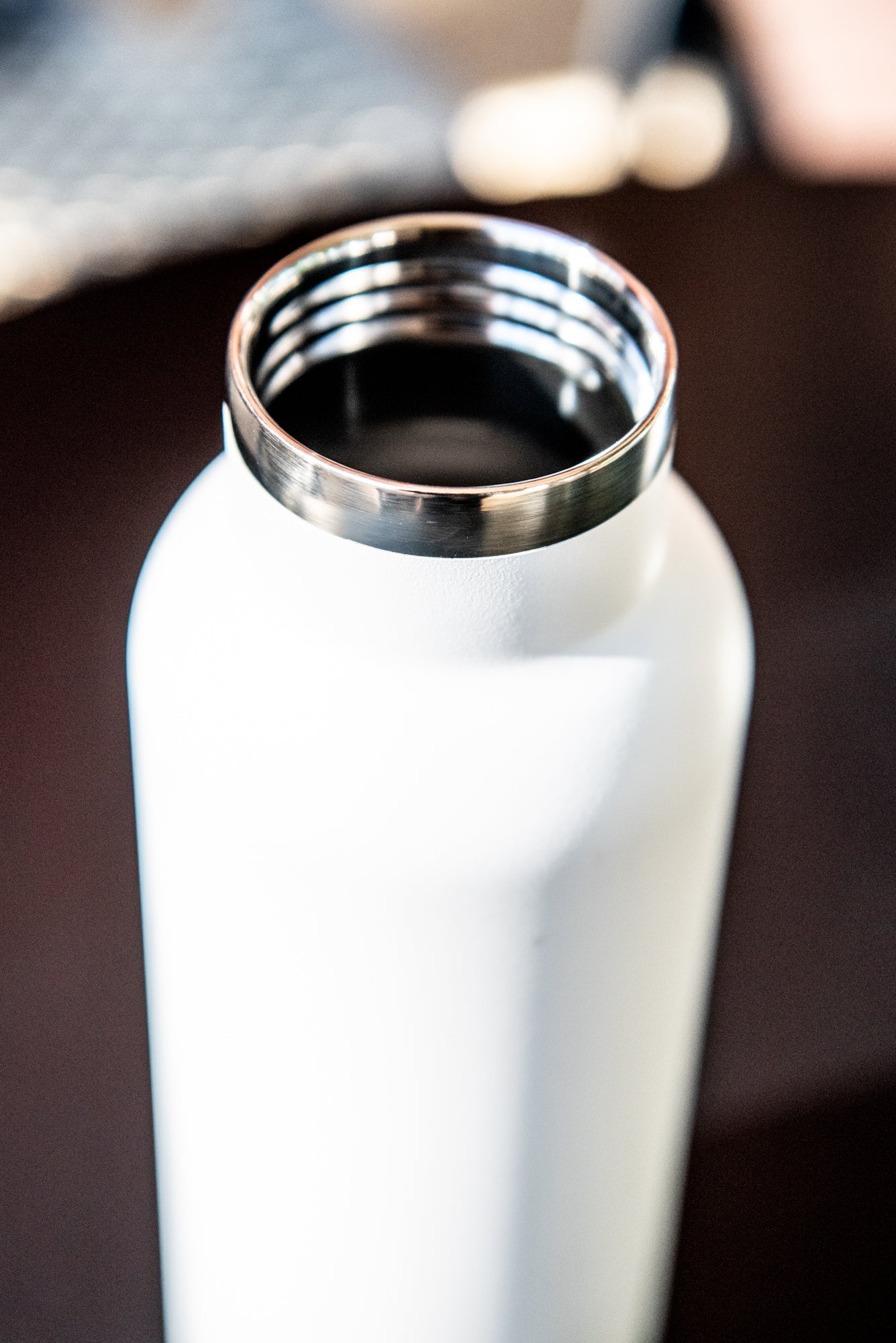 Top-down view of a white RMIT Store 600ml thermo bottle with the lid removed, revealing its stainless steel interior. The bottle is placed upright on a black tabletop.
