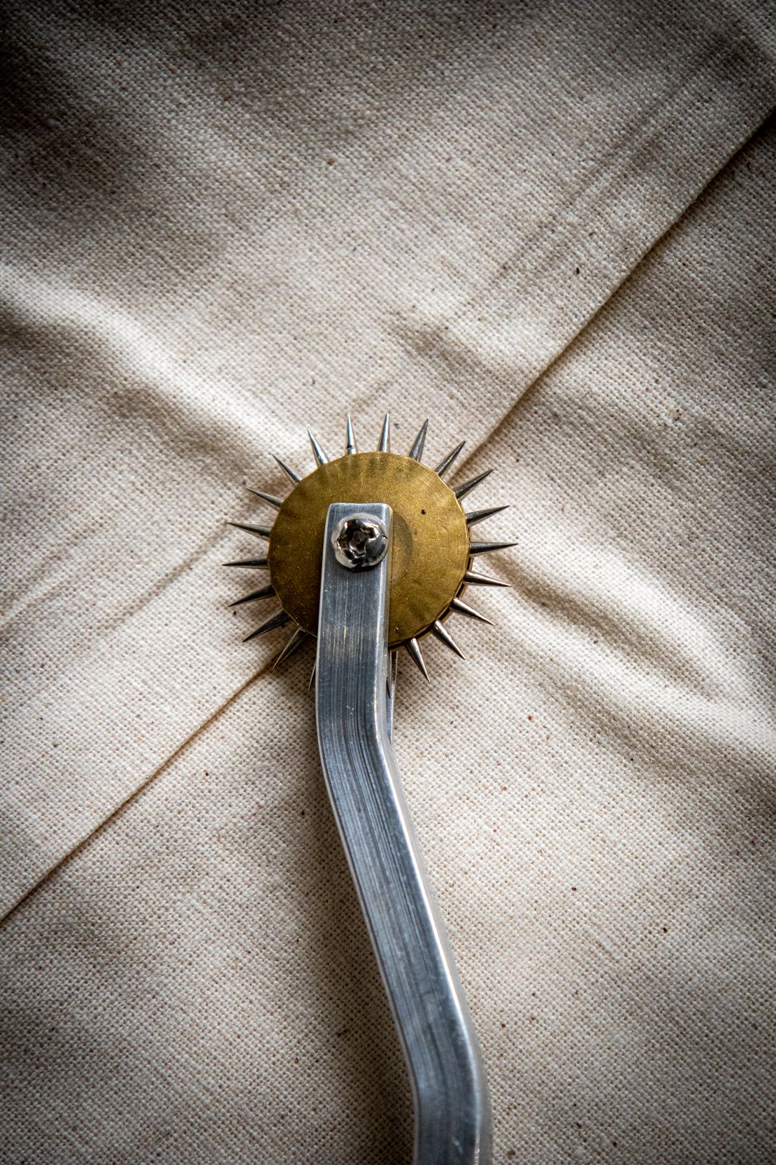 Angled view of a tracing wheel's exposed silver wheel resting diagonally on a light grey surface. Available from the RMIT Store.