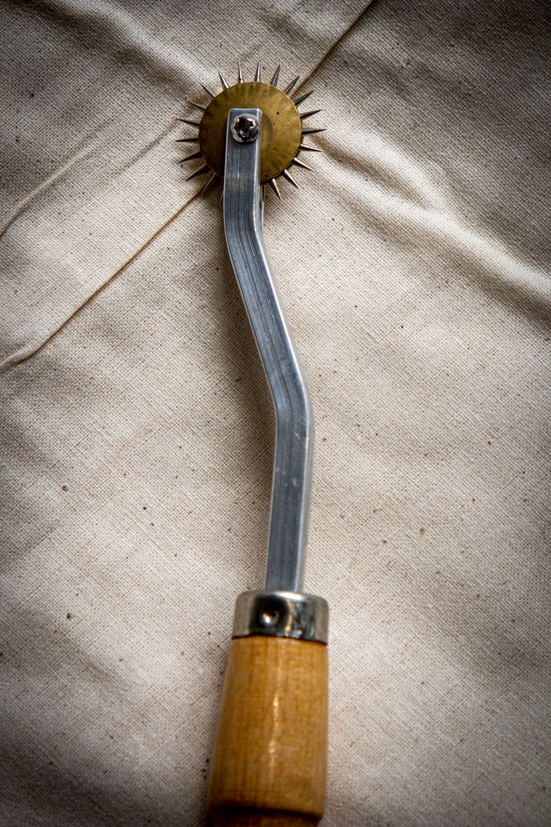 Close-up view of a tracing wheel with a wooden handle and silver metal wheel, positioned on a light grey surface. Sold by RMIT Store.