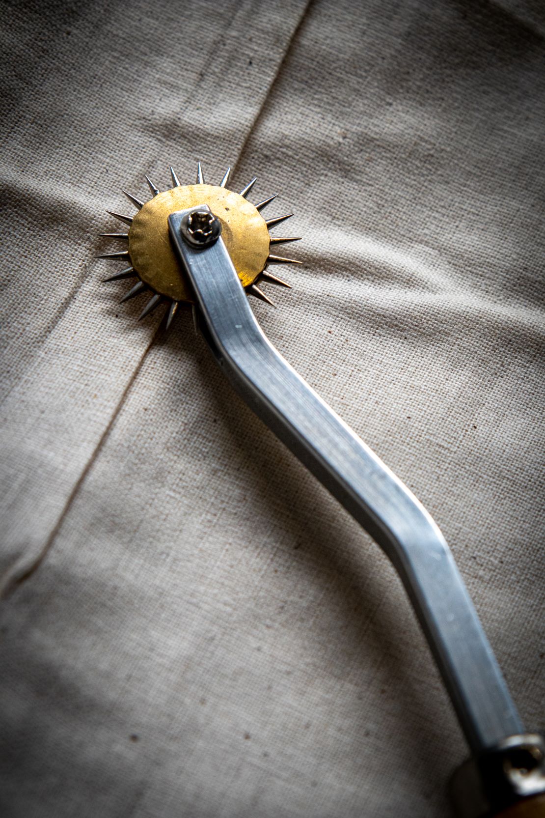 Top view of a tracing wheel's silver spiked wheel placed on a light grey surface. Available from the RMIT Store.