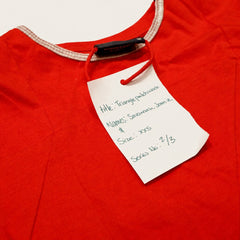 Triangle Patchwork fashion-student designed upcycled tee from RMIT Store, featuring a red upcycled short-sleeve tee with subtle reconstructed triangular and angled seam panels across the front while retaining a clean red overall appearance, shown in a close-up showing the attached white swing tag and nearby reconstructed fabric details on a light studio background.
