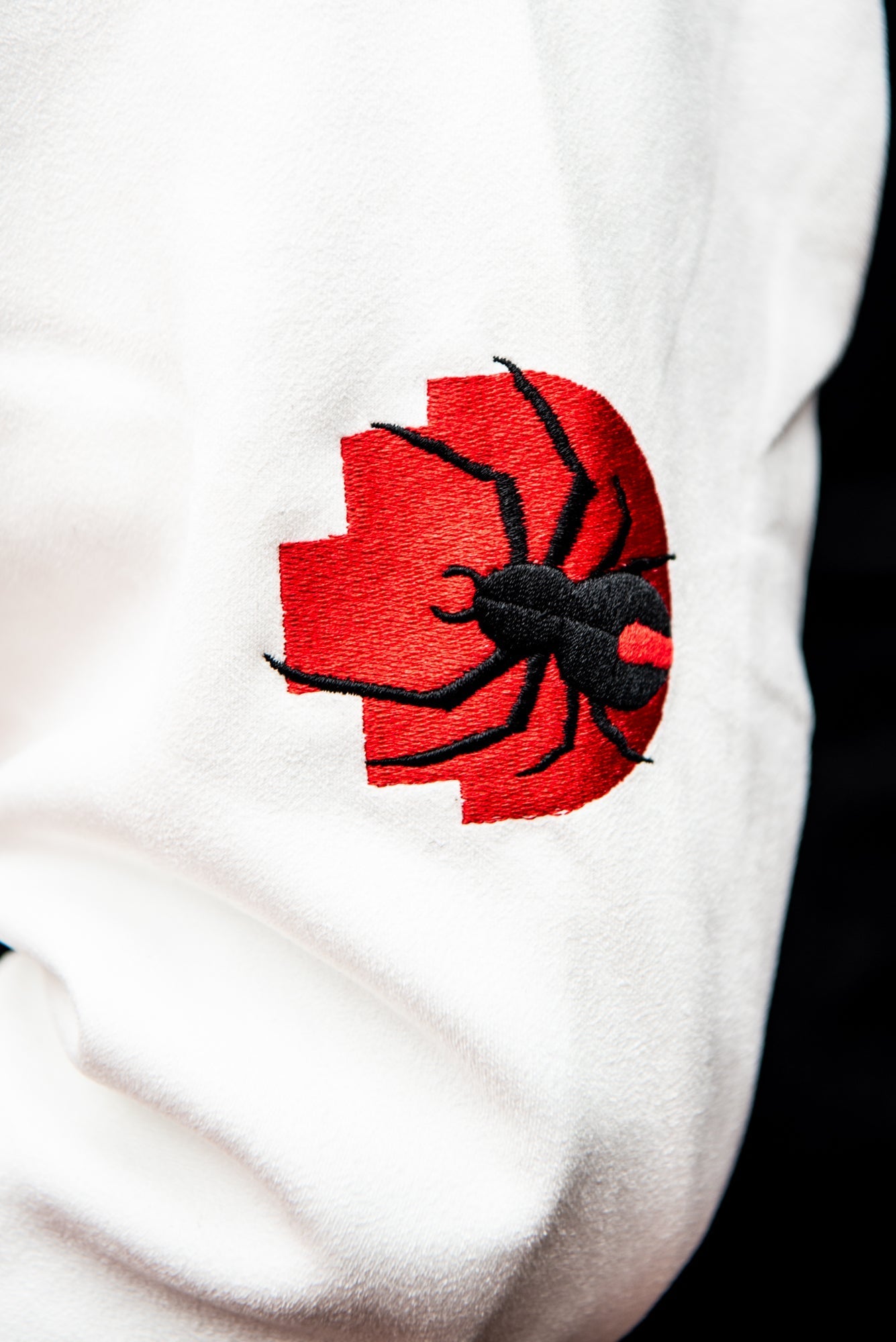 Close-up of a black spider design on a red pixelated background patch, stitched onto the white sleeve of the RMIT varsity jacket, available at the RMIT Store.