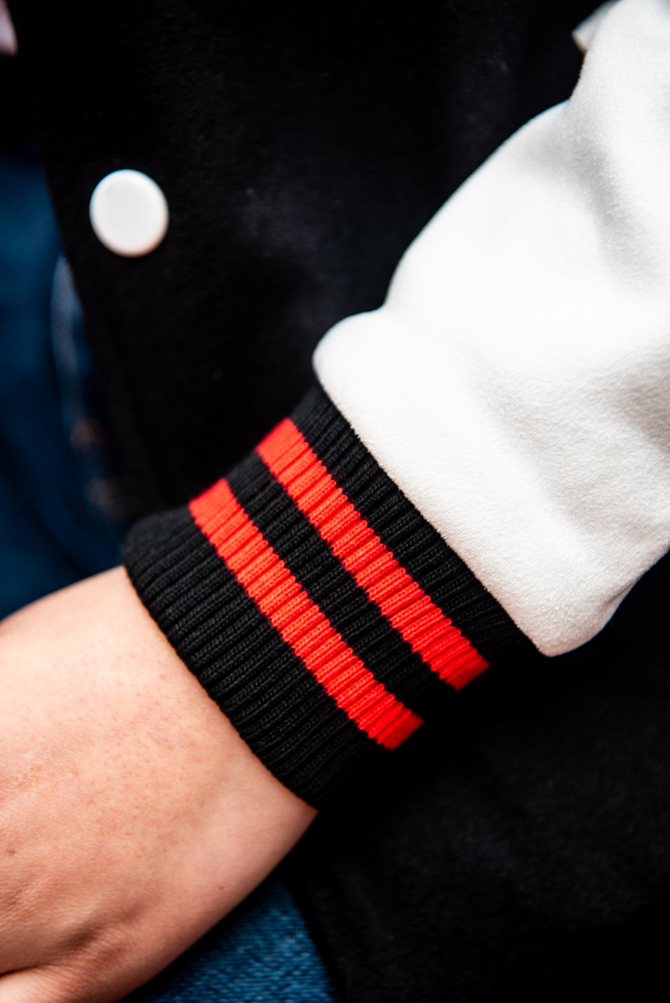 Close-up view of the sleeve of a black and white RMIT varsity jacket, showing the white main sleeve area with a black cuff trimmed with a red line, available at the RMIT Store.
