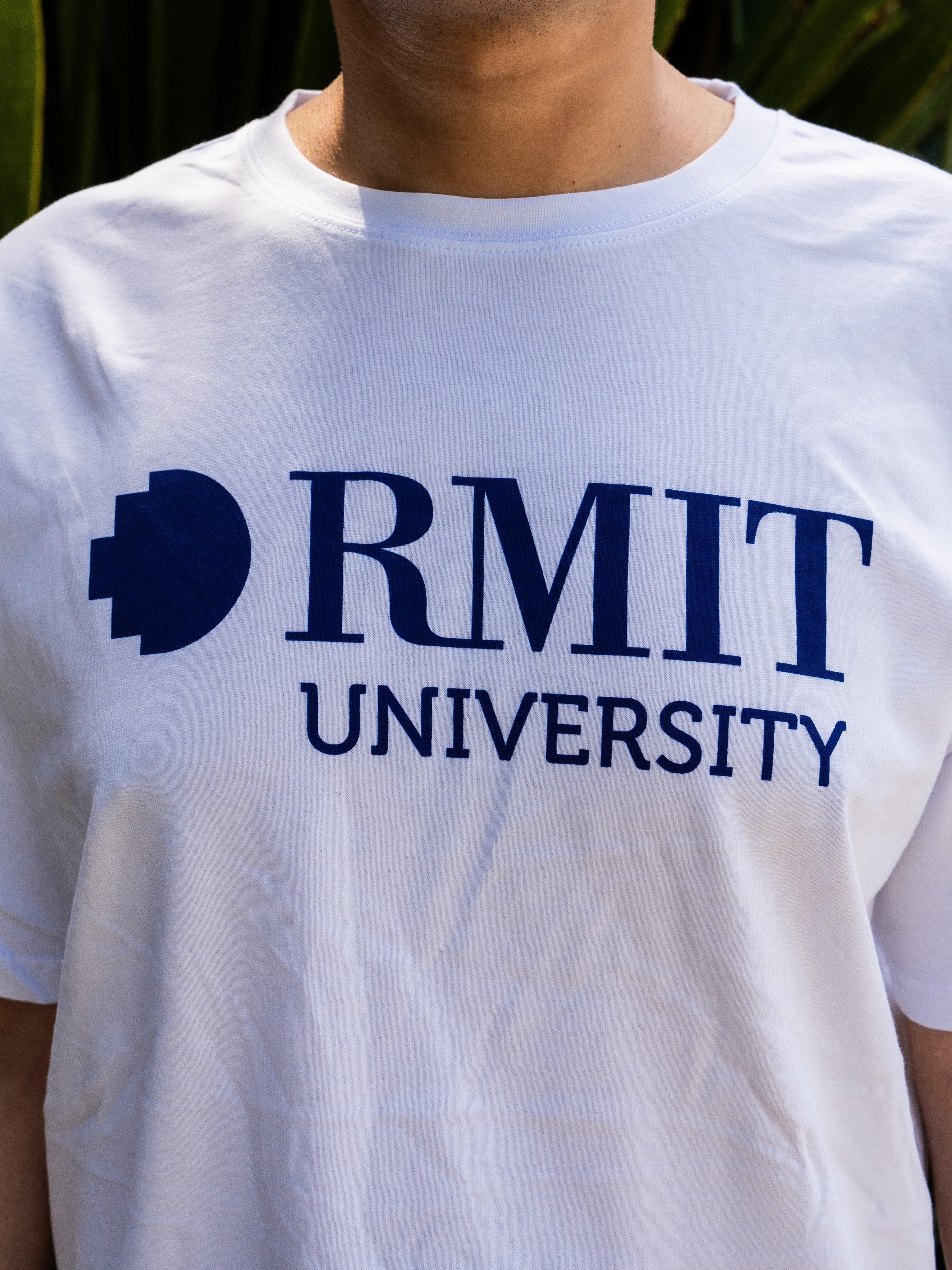 Close-up of a plain white RMIT Welcome tee from the RMIT Store, featuring a bold blue RMIT logo printed prominently in the centre of the chest. 