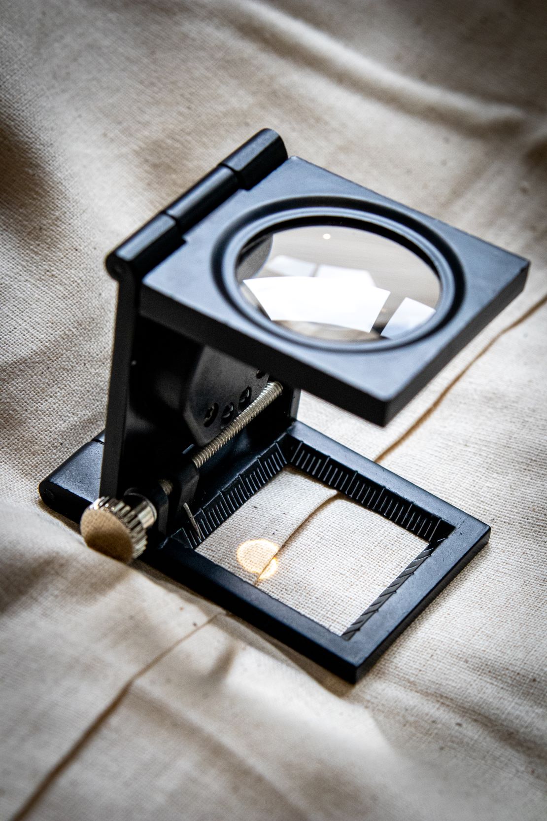 Side view of black yarn thread counter in a folded position, highlighting the compact design and matte black finish, with the square glass panel edge faintly visible. Item is positioned on a light grey surface for RMIT Store.