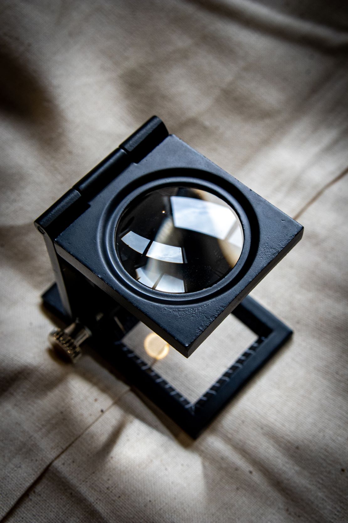 Black yarn thread counter viewed from a slightly elevated angle, showing the open rectangular frame with a transparent glass viewing panel on top and measurement markings faintly visible inside. Displayed on a light grey surface for RMIT Store.