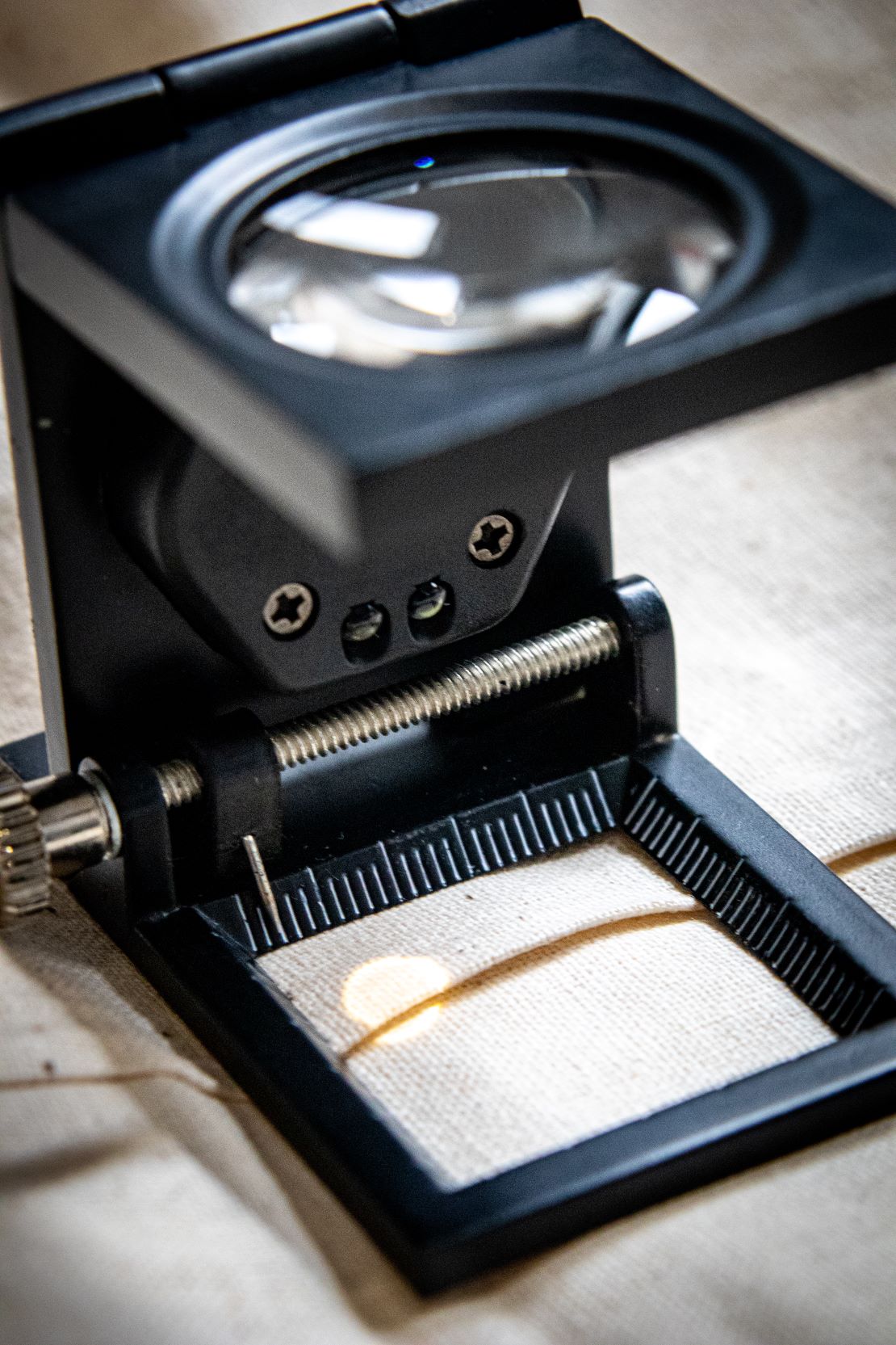Black yarn thread counter with a square frame and a transparent glass viewing window on top, designed for counting yarn threads through magnification. The tool is made of matte black material and positioned upright on a light beige surface for RMIT Store.