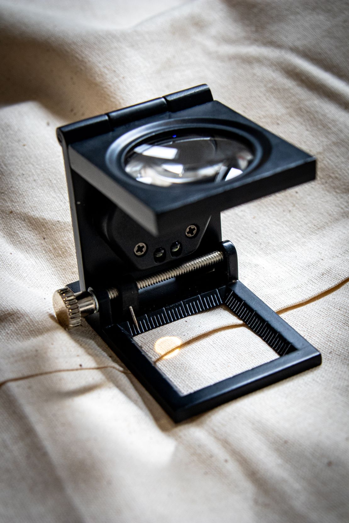 Black yarn thread counter with a square frame and a transparent glass viewing window on top, designed for counting yarn threads through magnification. The tool is made of matte black material and positioned upright on a light grey surface for RMIT Store.