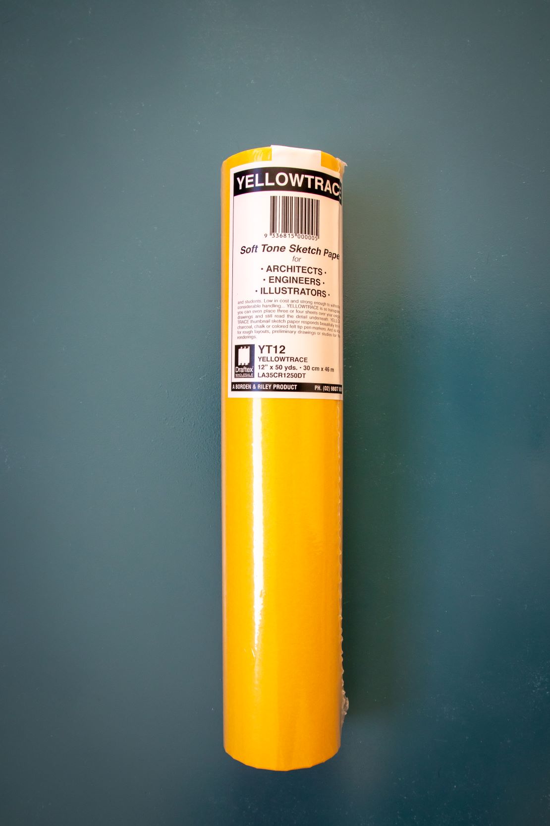 Full view of a yellow trace paper roll standing upright on a plain teal background. Available at the RMIT Store.
