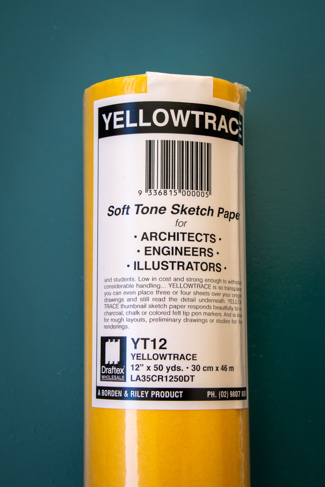 Close-up of the upper section of a yellow trace paper roll showing product details, displayed on a plain teal background. Available at the RMIT Store.