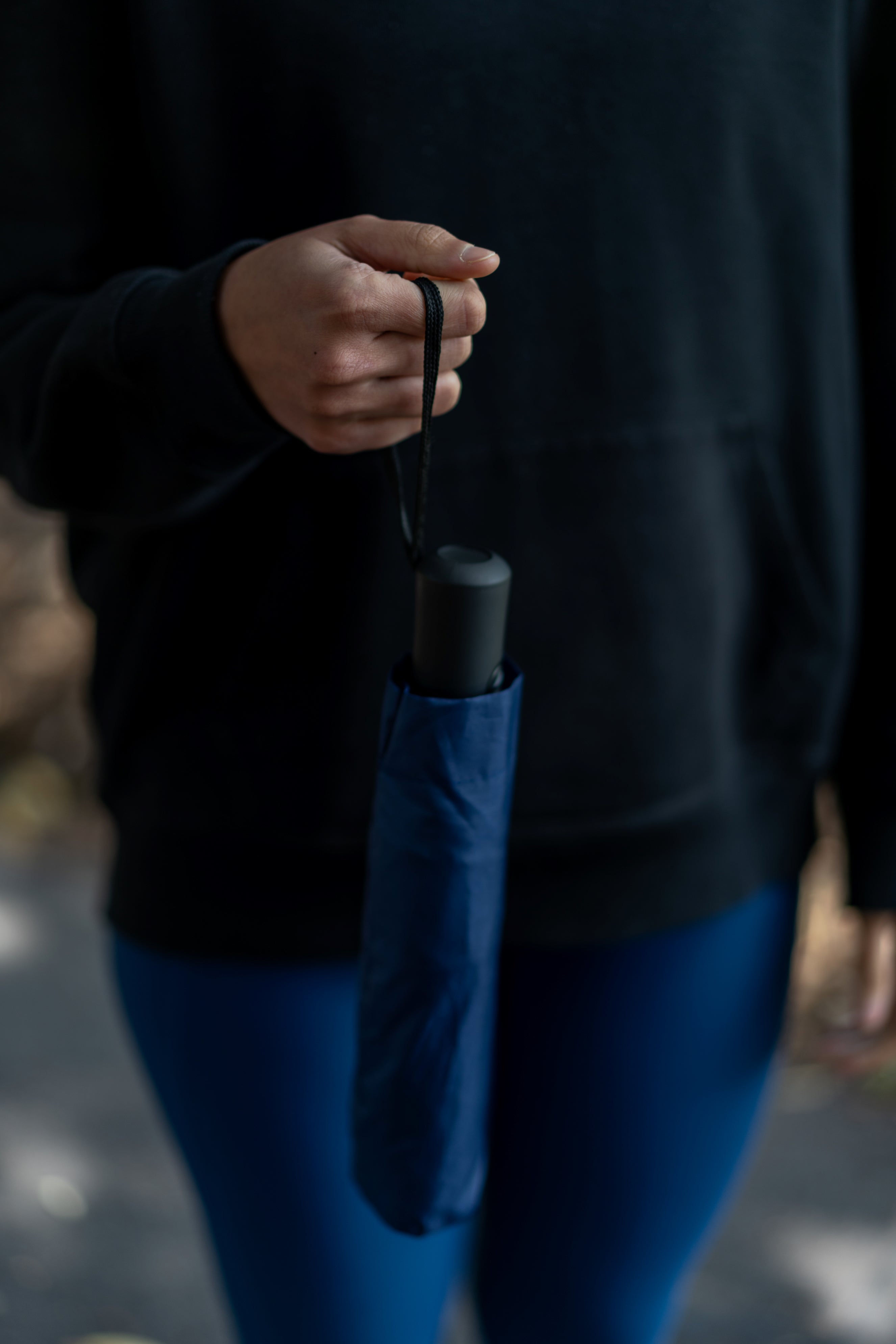 The RMIT Store Compact Umbrella in Navy being held by the wrist loop while fully packed in its cover.