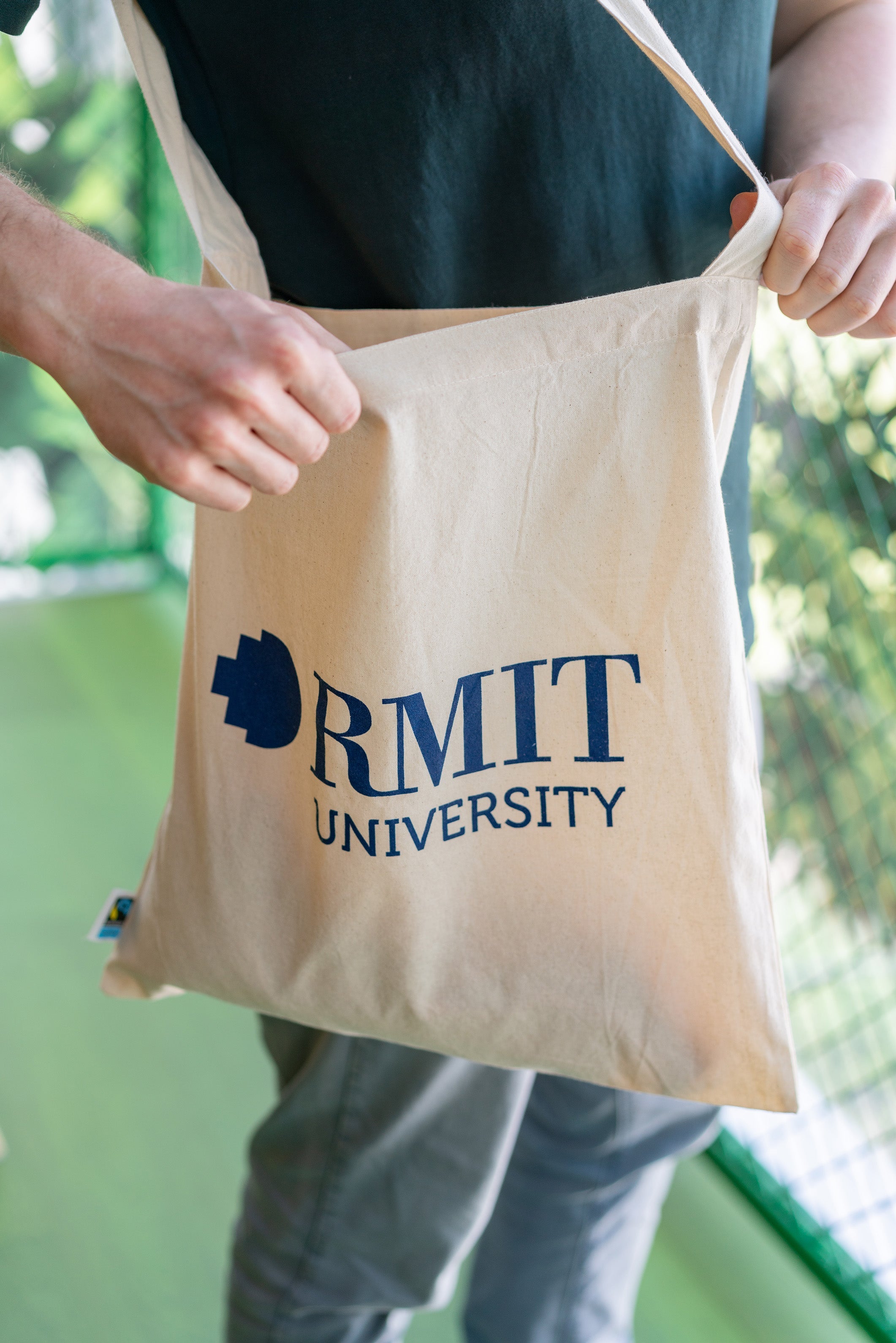 The RMIT Store Fairtrade Cotton Tote with the RMIT University logo in RMIT Blue colour. Modelled by male.