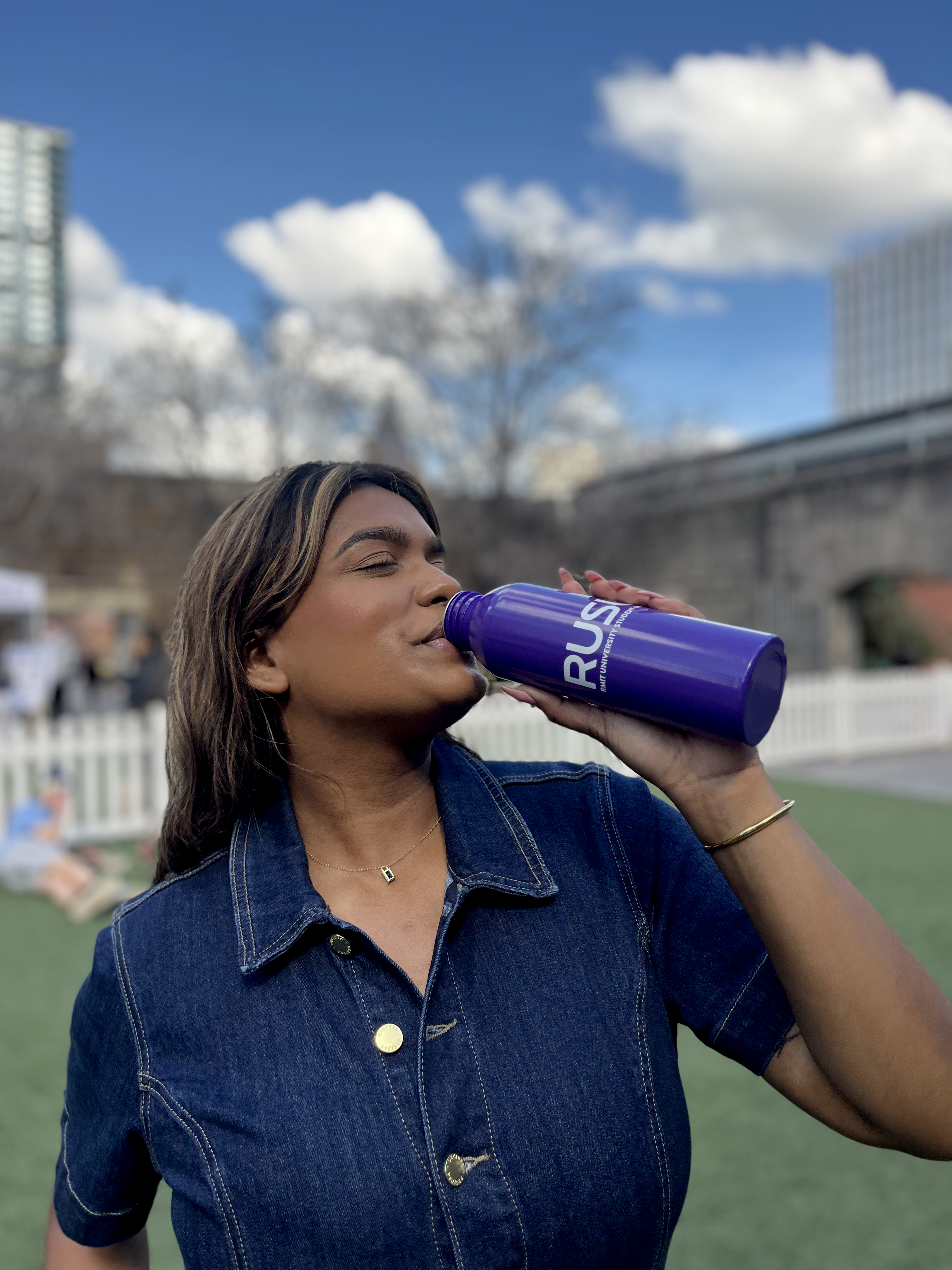 RUSU Water Bottle in puprple with a white printerd RUSU logo. Female student drinking from the bottle.