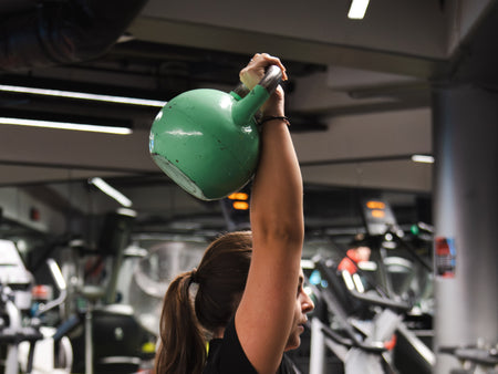 female performing a kettlebell overhead press exercise in gym
