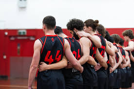 Team of basketball players in red and black uniforms huddled together on a court for the RMIT Redbacks Big V team.