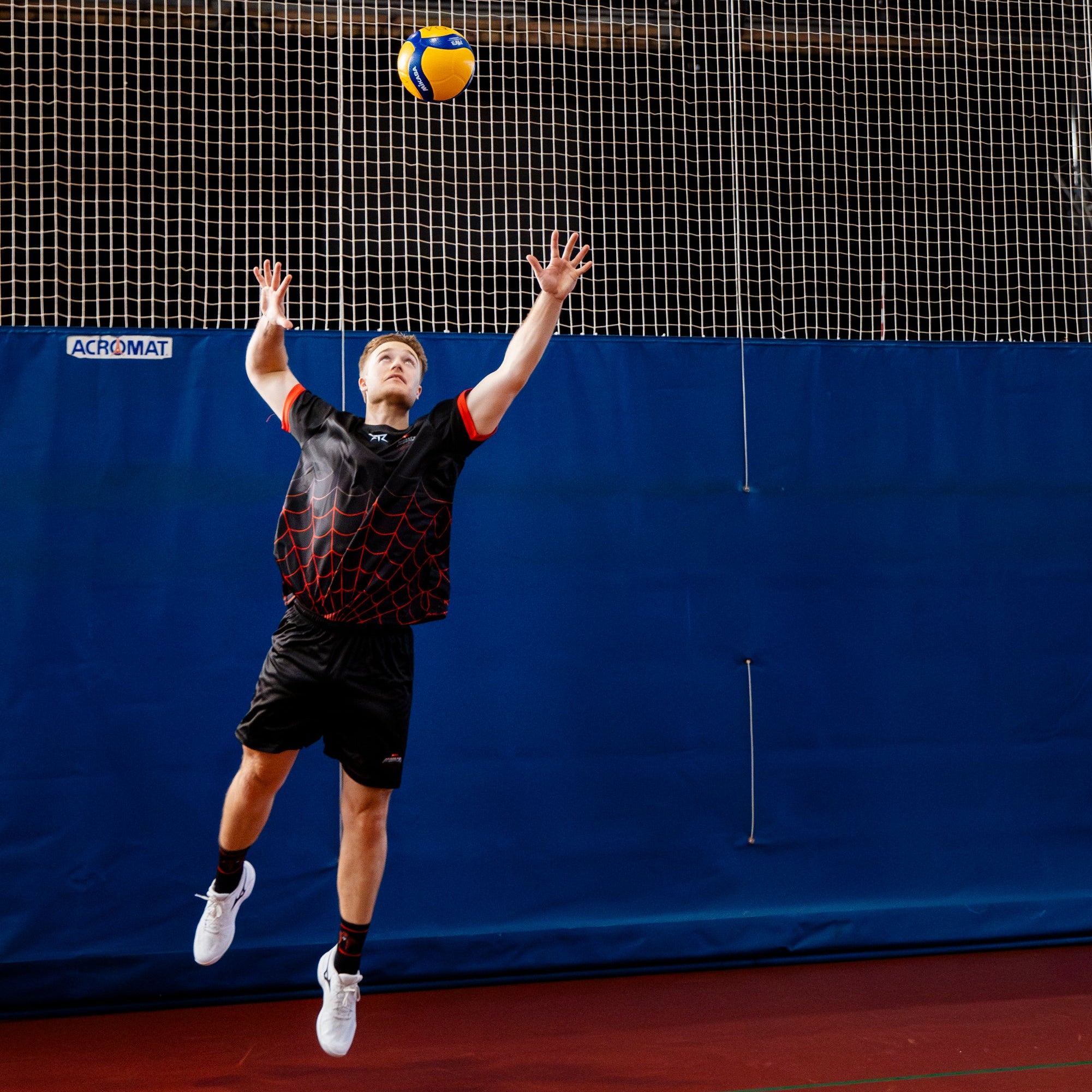 Person playing volleyball indoors with a blue wall and net in the background for the RMIT Redbacks