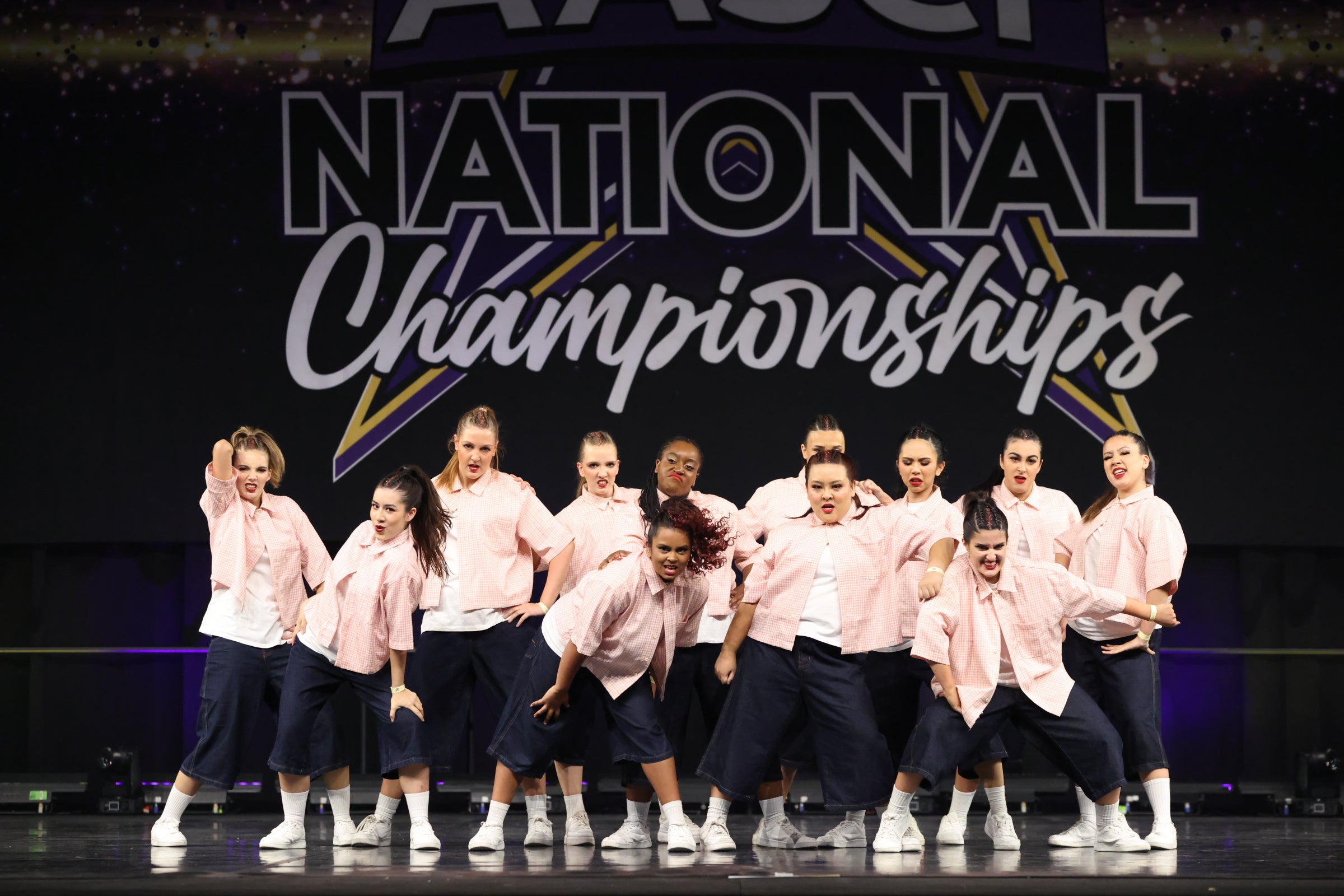 Group of RMIT Cheer and Dance dancers in matching outfits on a stage with 'National Championships' text in the background