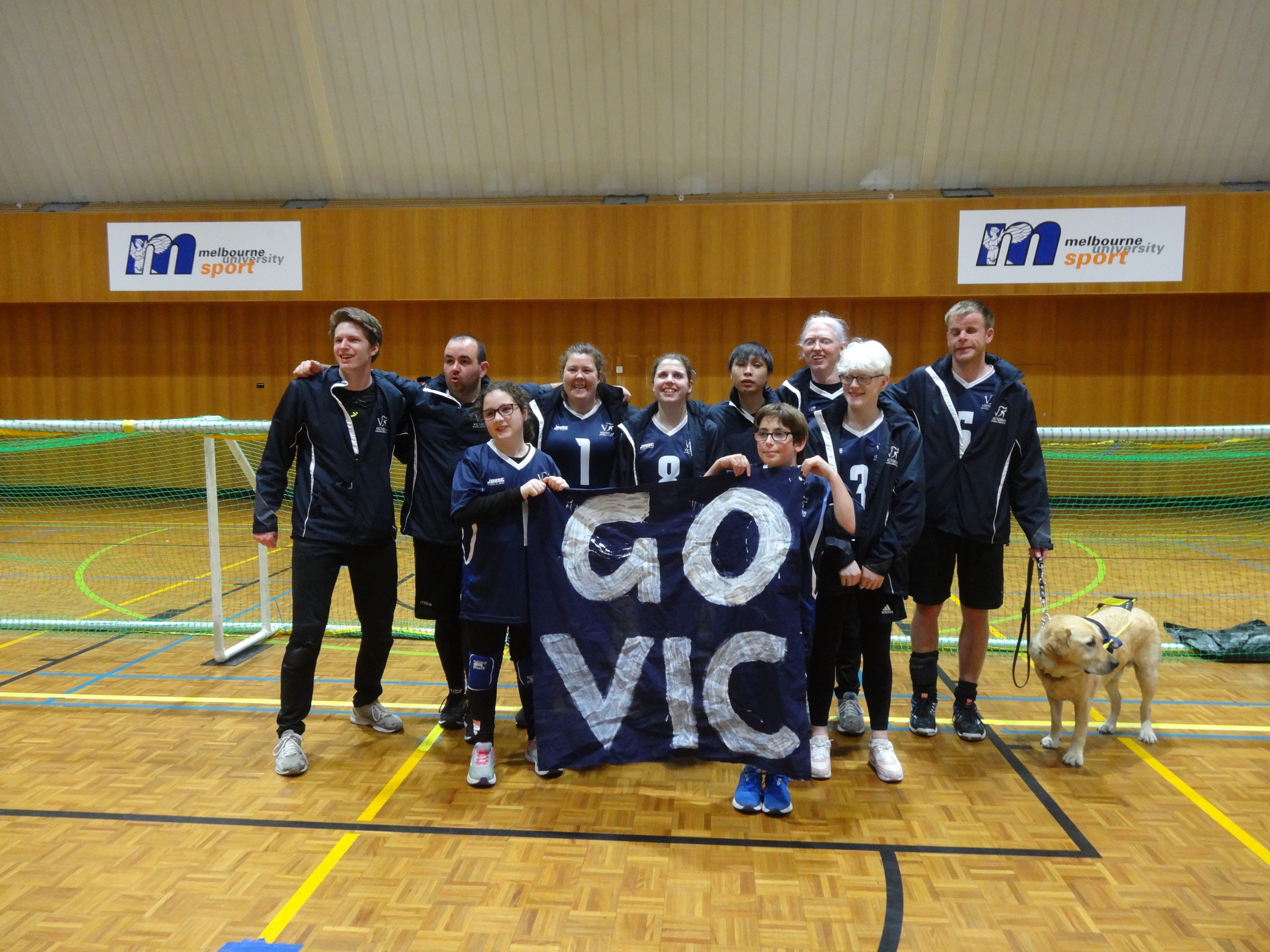 Goalball team posing with 'Go Vic' banner