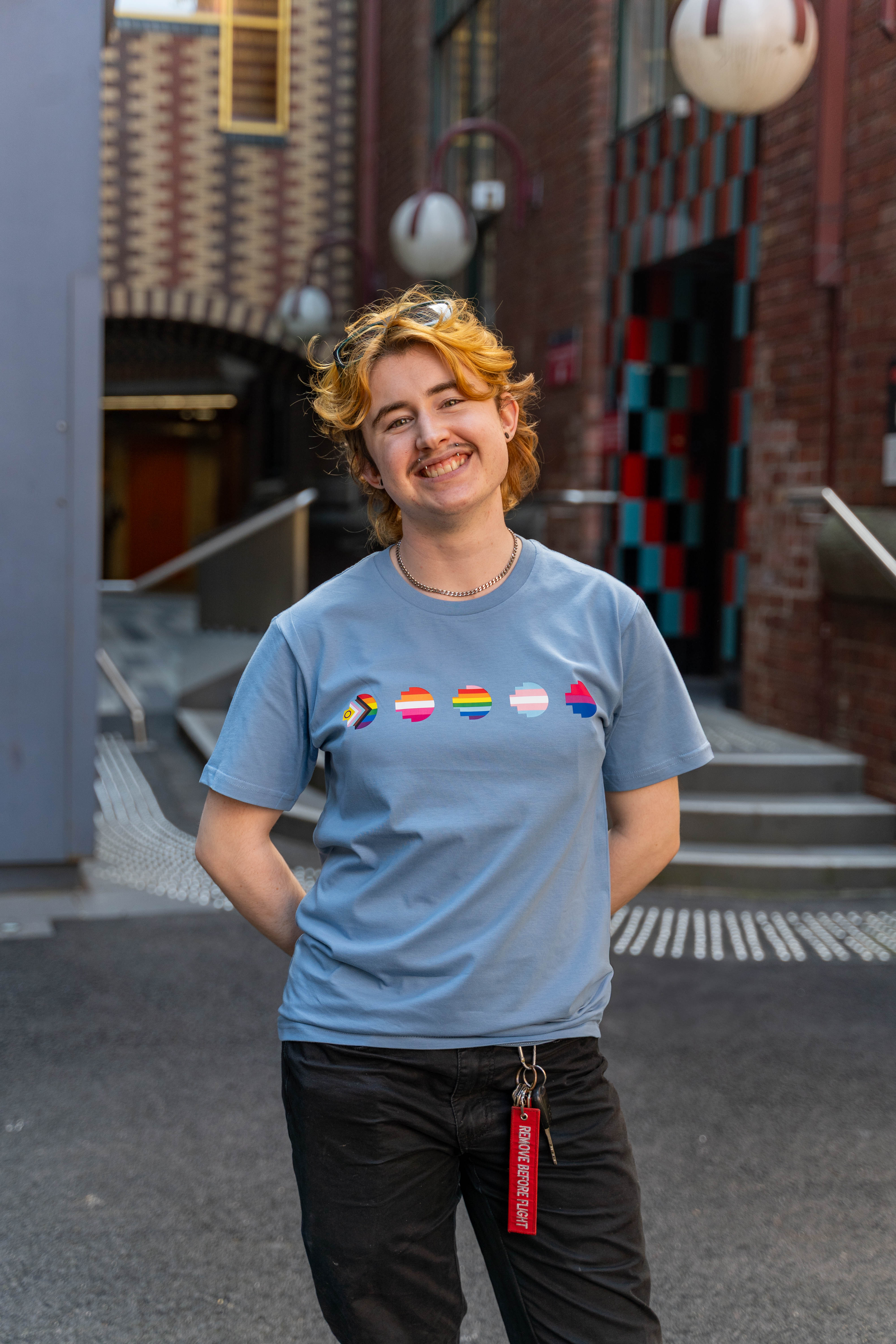 Front view of a smiling model wearing the limited edition blue Pride Unity Tee from RMIT Store, showcasing pride flag designs emblazoned across the chest in a colourful format.
