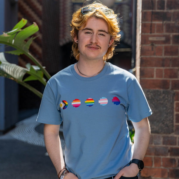 Modelled front view of the limited edition blue Pride Unity Tee from RMIT Store, displaying pride flags in a row across the chest in a contemporary urban backdrop.