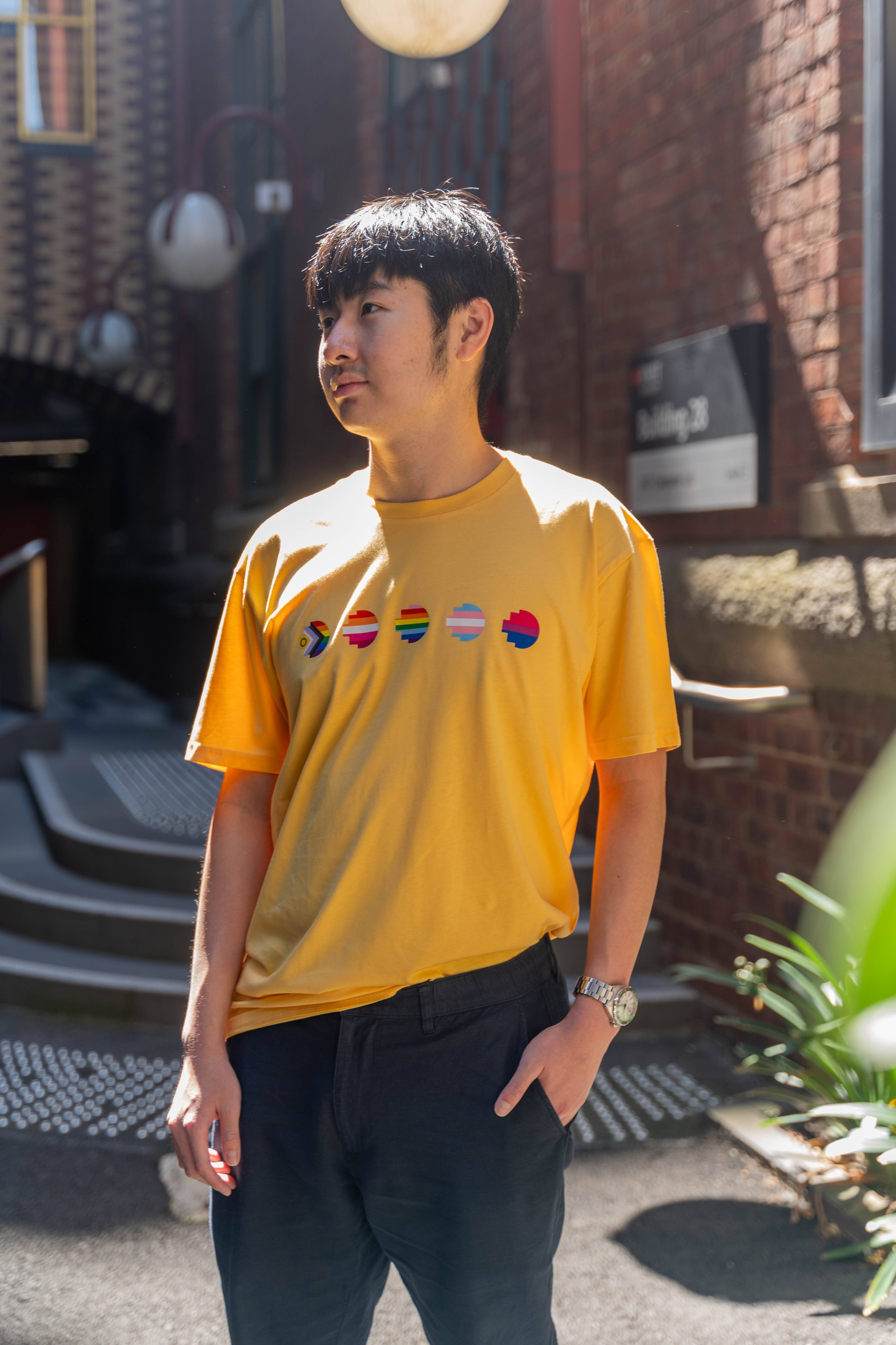 Side angle of model in the limited edition yellow Pride Unity Tee from RMIT Store, showcasing vivid pride flag designs and casual fit.